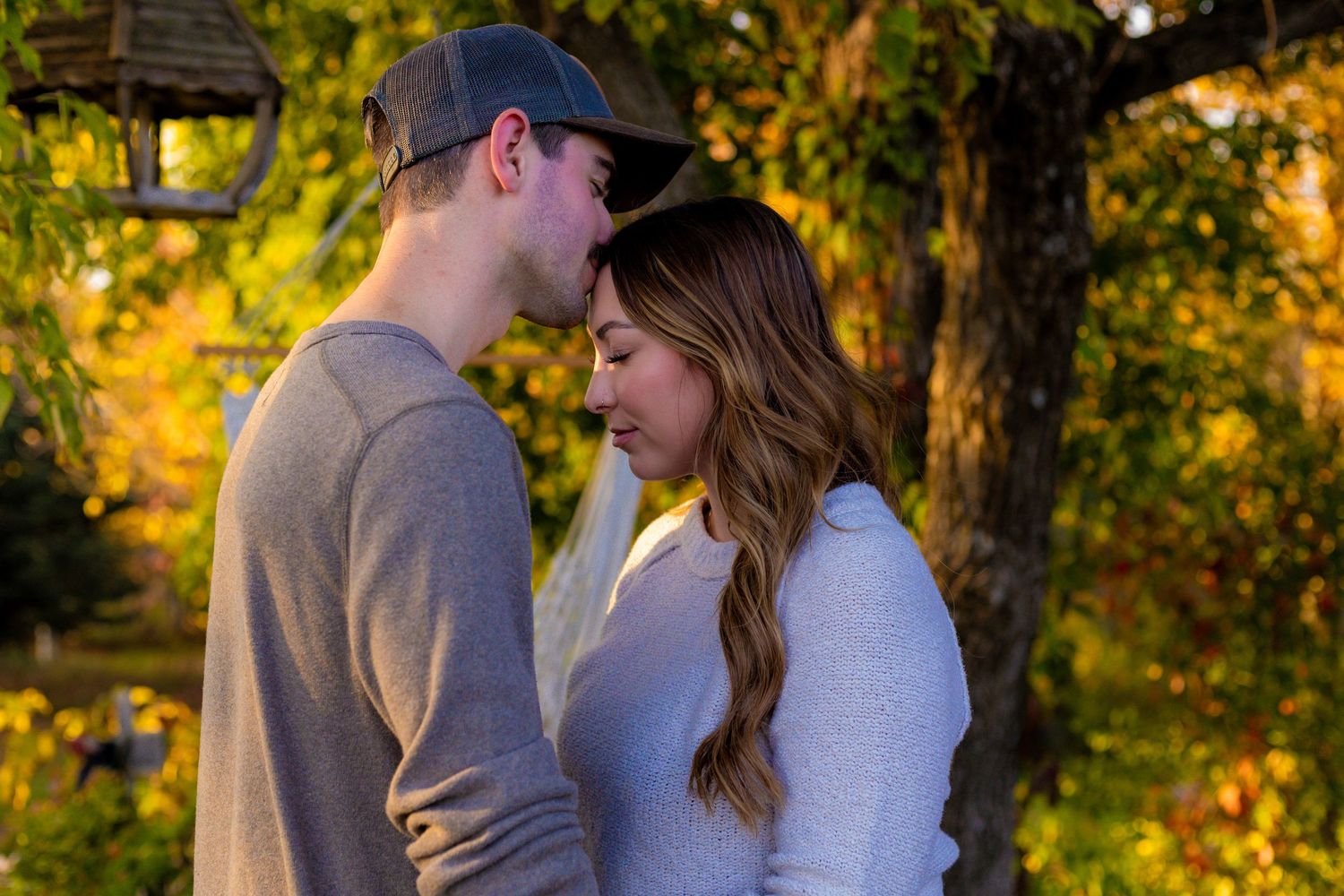 Couple sharing intimate forehead touch moment surrounded by golden autumn foliage.