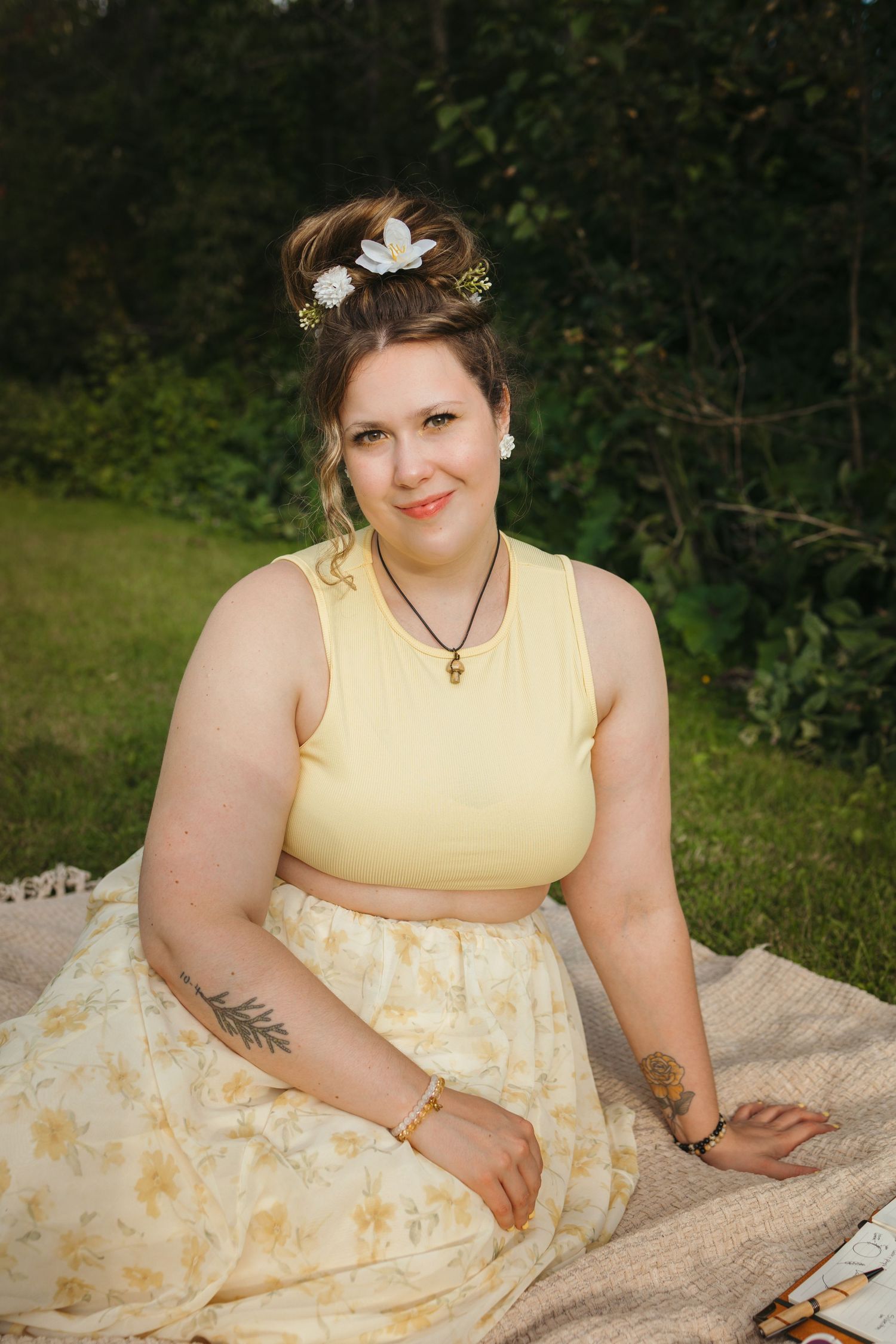 Woman in yellow crop top and floral skirt sitting on blanket outdoors with flowers in her hair.