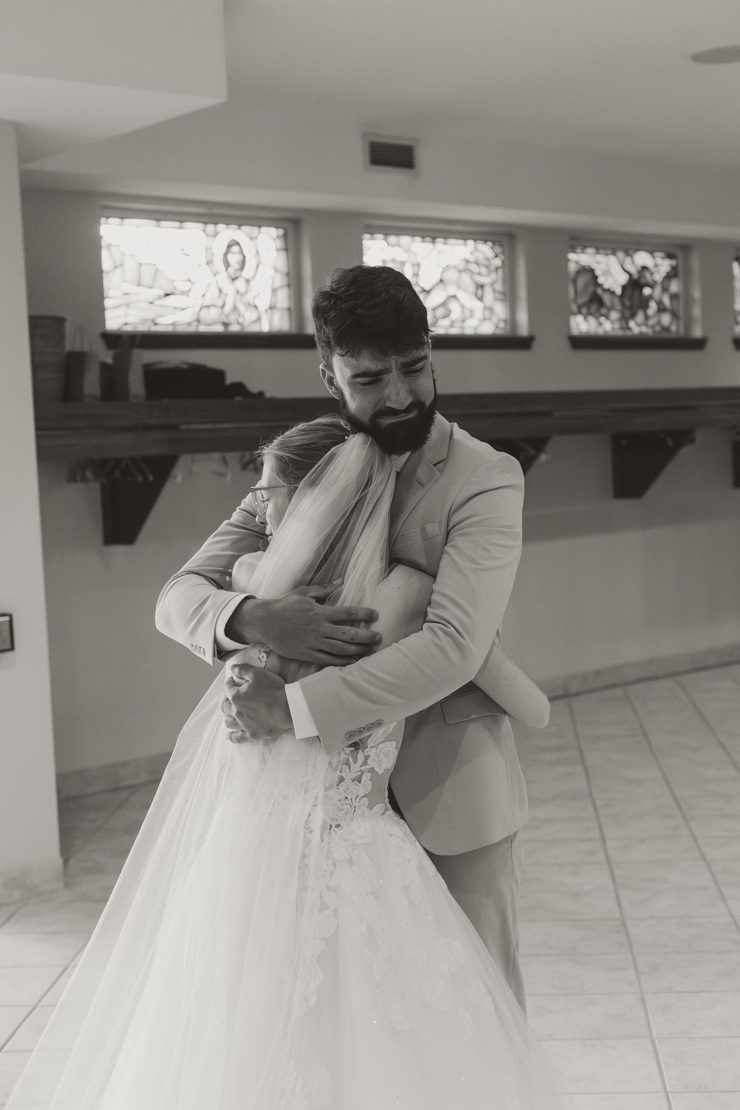 Emotional black and white photo of groom embracing bride tightly during their wedding day in a church.