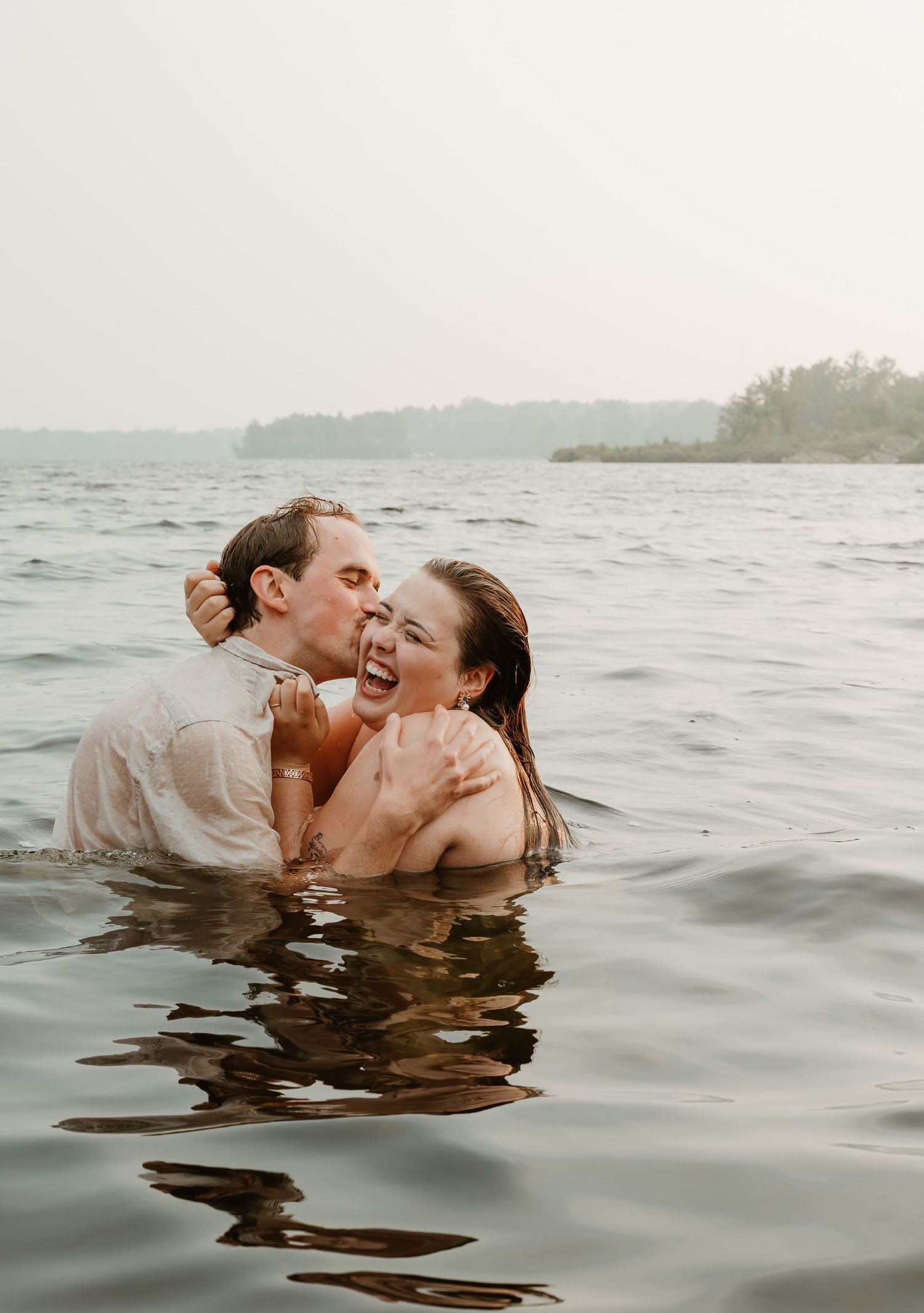 Joyful couple laughing and embracing while swimming in serene lake together.