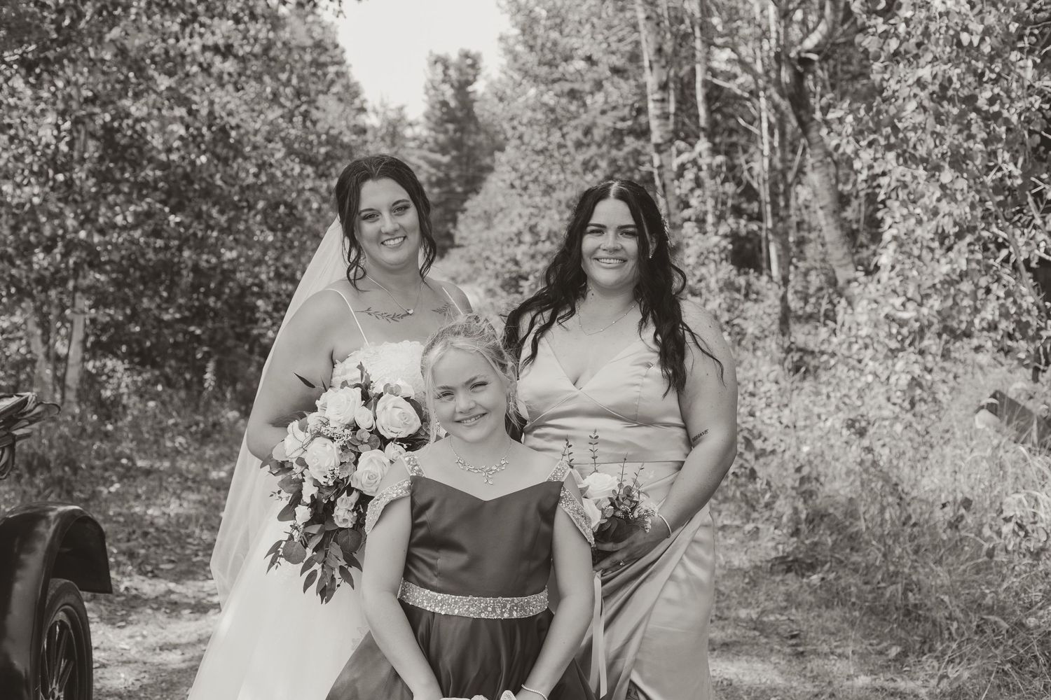 A bride with bouquet poses with a bridesmaid and flower girl in a black and white photo.