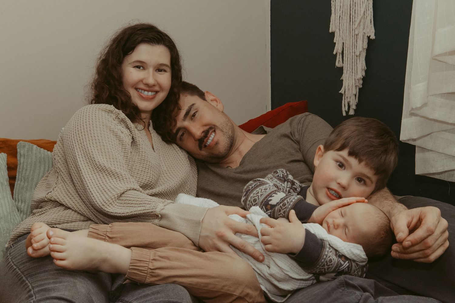 Joyful family of four with newborn baby and toddler relaxing together on a cozy couch.