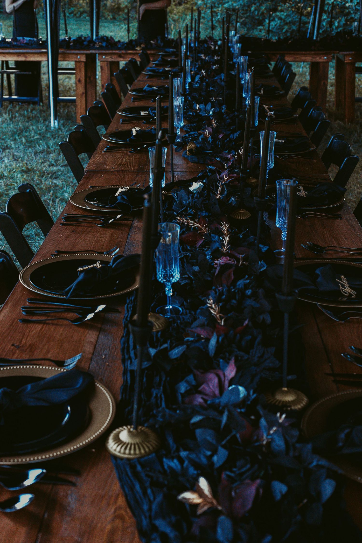 Elegant dark wedding reception table with navy blue florals and black taper candles.