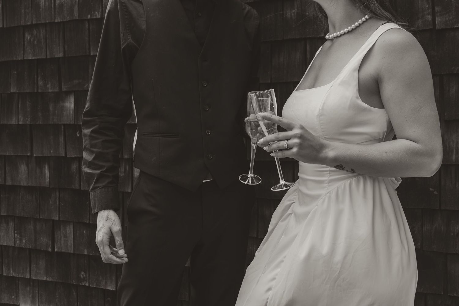 Bride in white dress and groom in black suit holding champagne flutes, black and white photo.