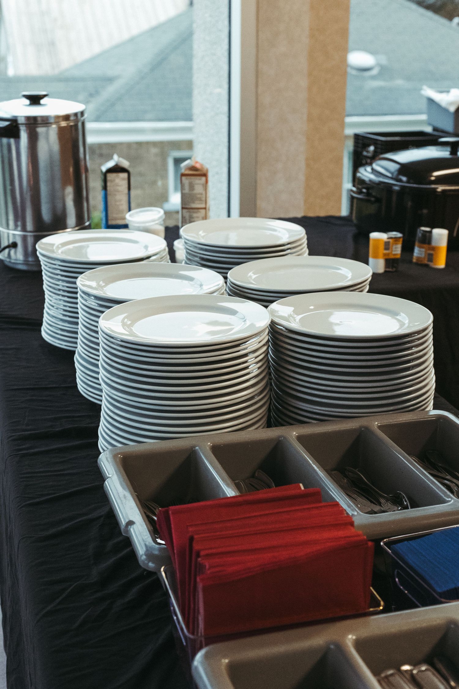 Stacked white dinner plates with red napkins and cutlery organized in a catering setup for an event.