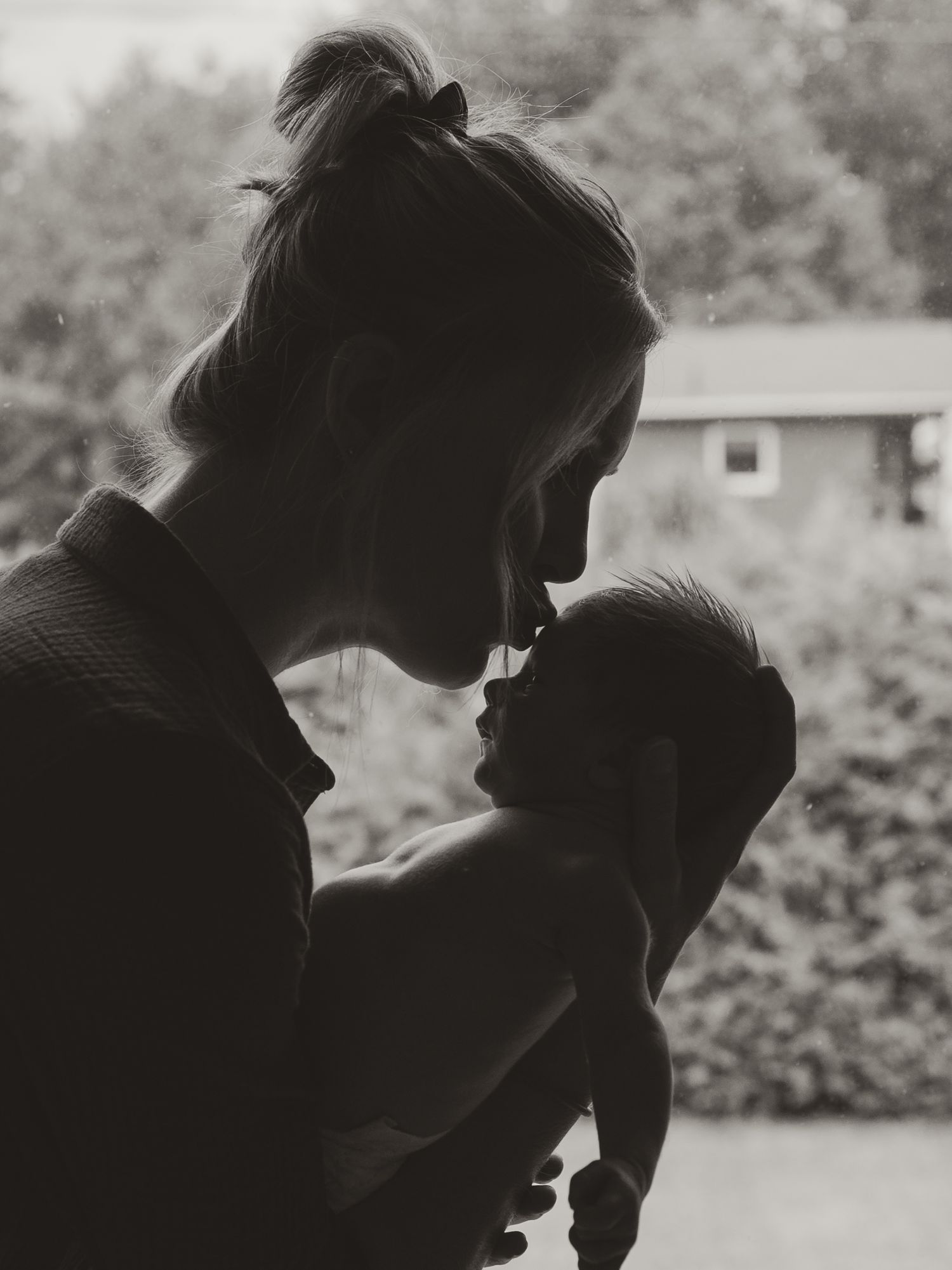 Black and white silhouette of a mother tenderly holding and gazing at her newborn baby by a window.