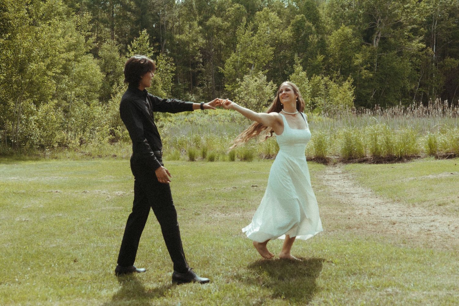 Joyful couple dancing and spinning together on a green lawn surrounded by trees.
