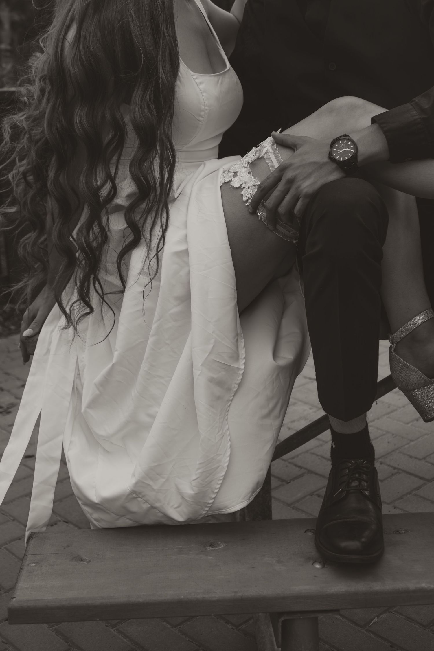 Bride in white dress with curly hair sitting beside groom in black suit, black and white photo.