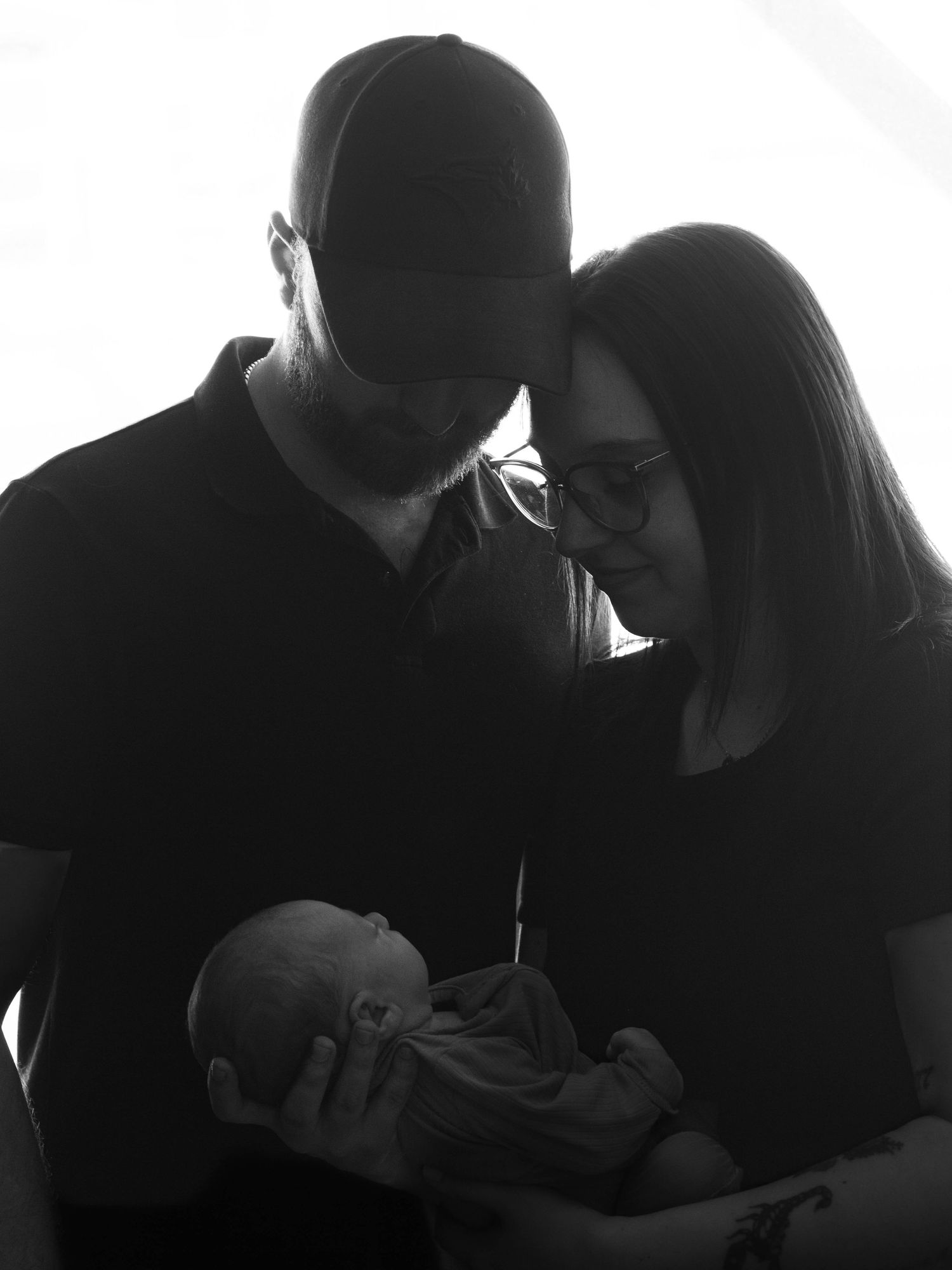 Black and white silhouette of parents with baseball cap tenderly holding their newborn baby.