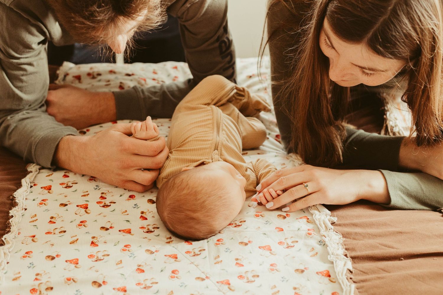 Parents' hands gently touching their newborn baby lying on a floral blanket.
