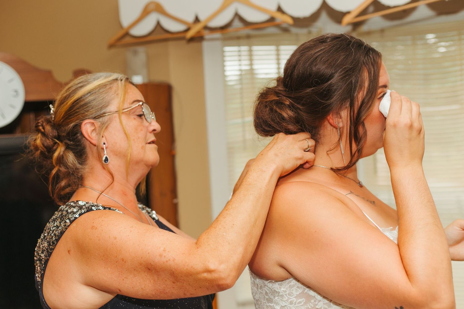Woman helping bride with necklace while getting ready for wedding ceremony.