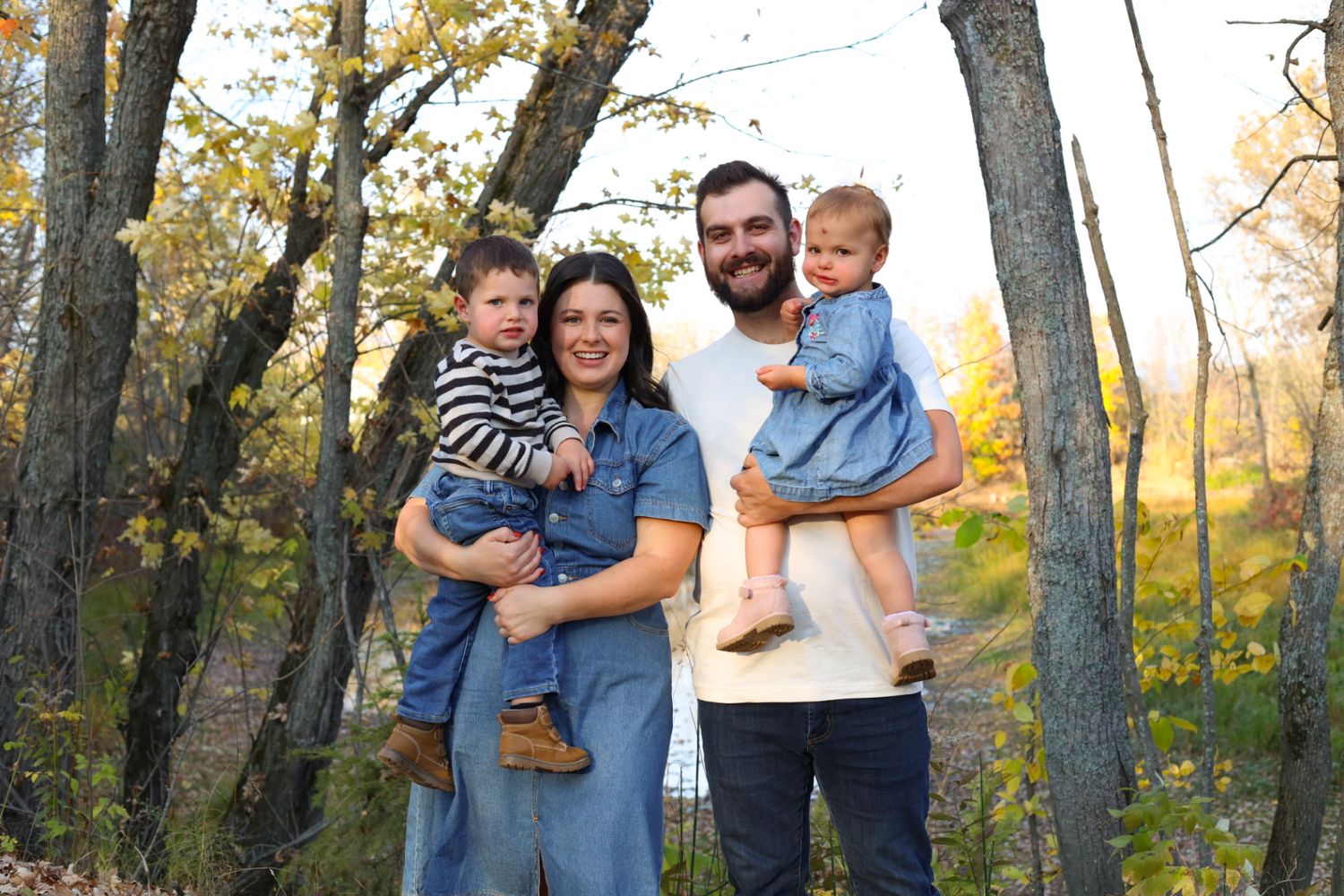 Happy family of four smiling together among colorful autumn trees in a forest setting.
