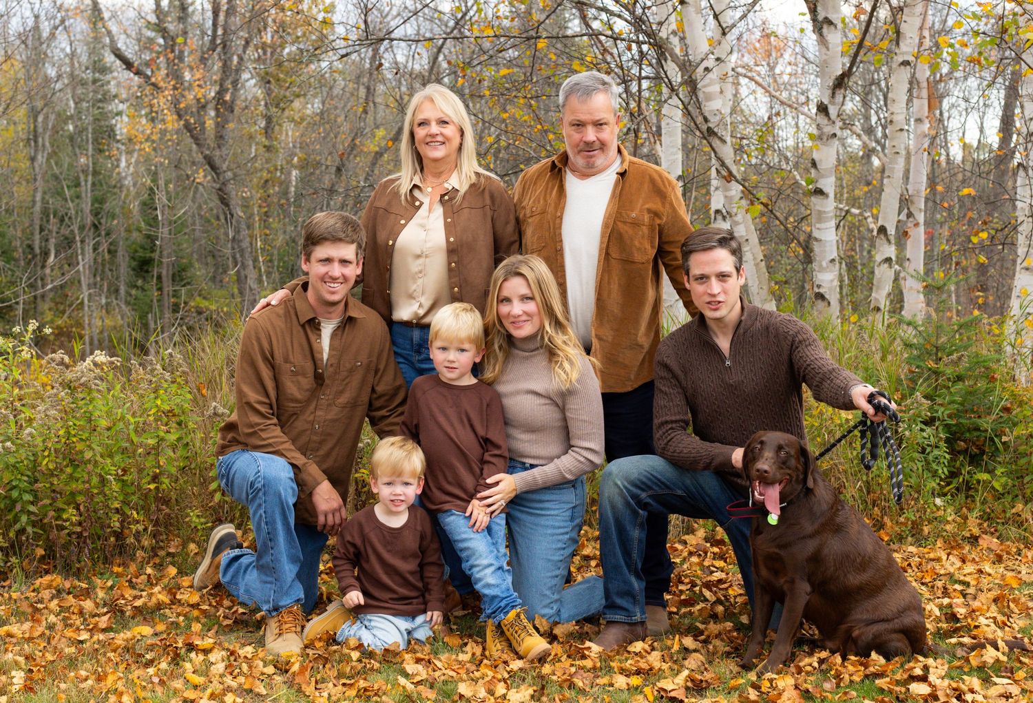 Extended family with dog poses together in colorful autumn leaves in the woods.
