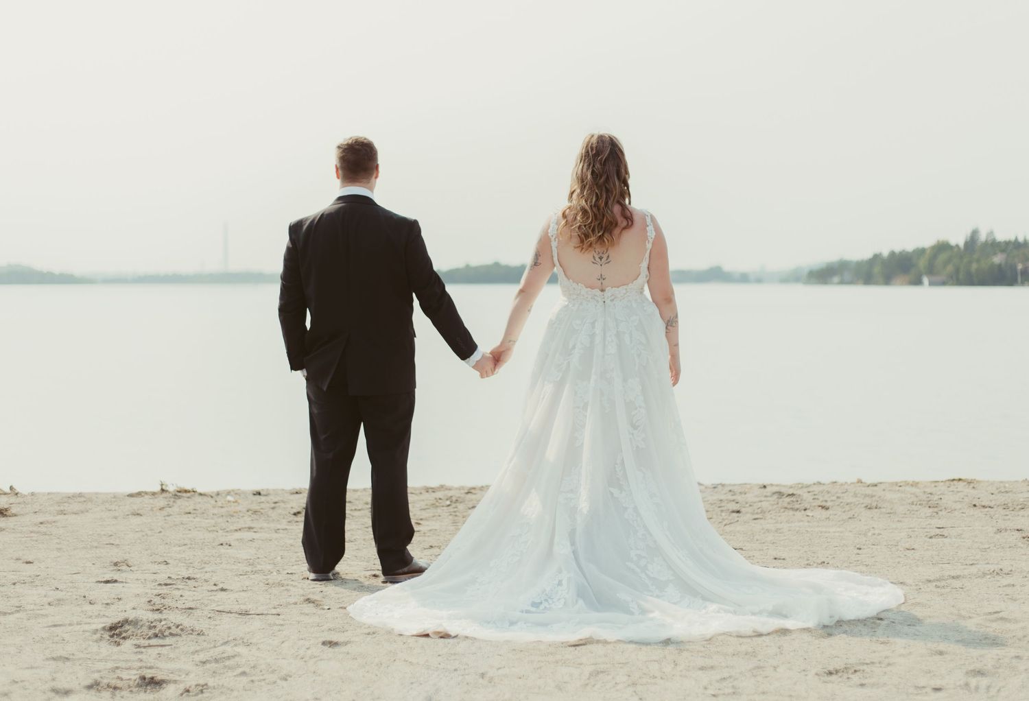 Bride in blue wedding gown and groom in black suit holding hands on sandy beach.