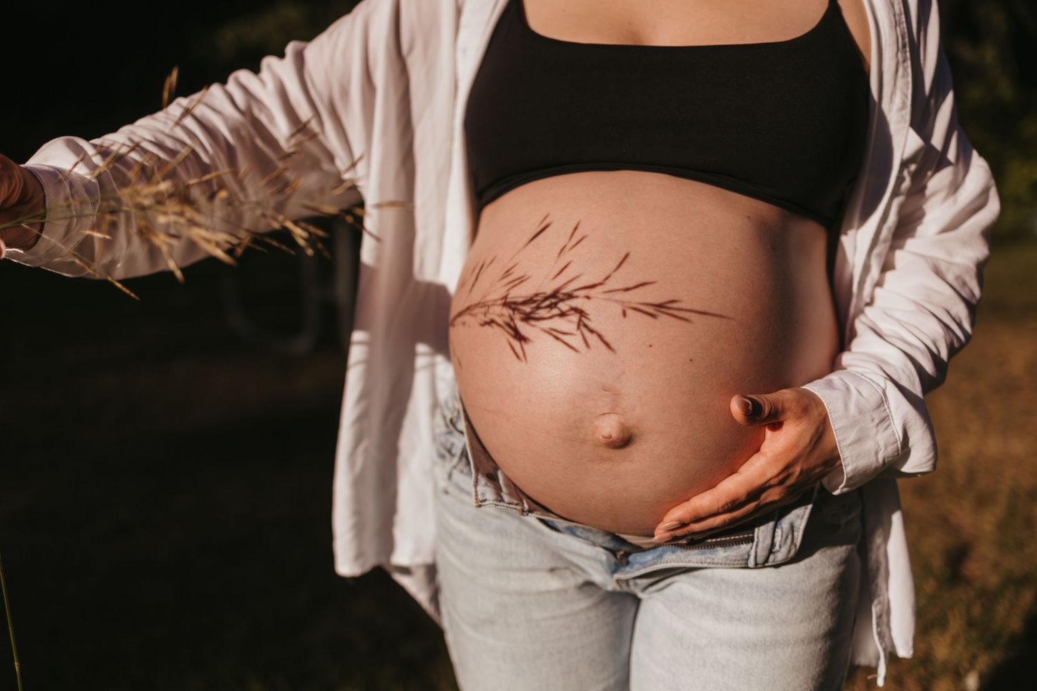 Pregnant woman in black crop top and jeans holding her bare belly with a floral design painted on it.
