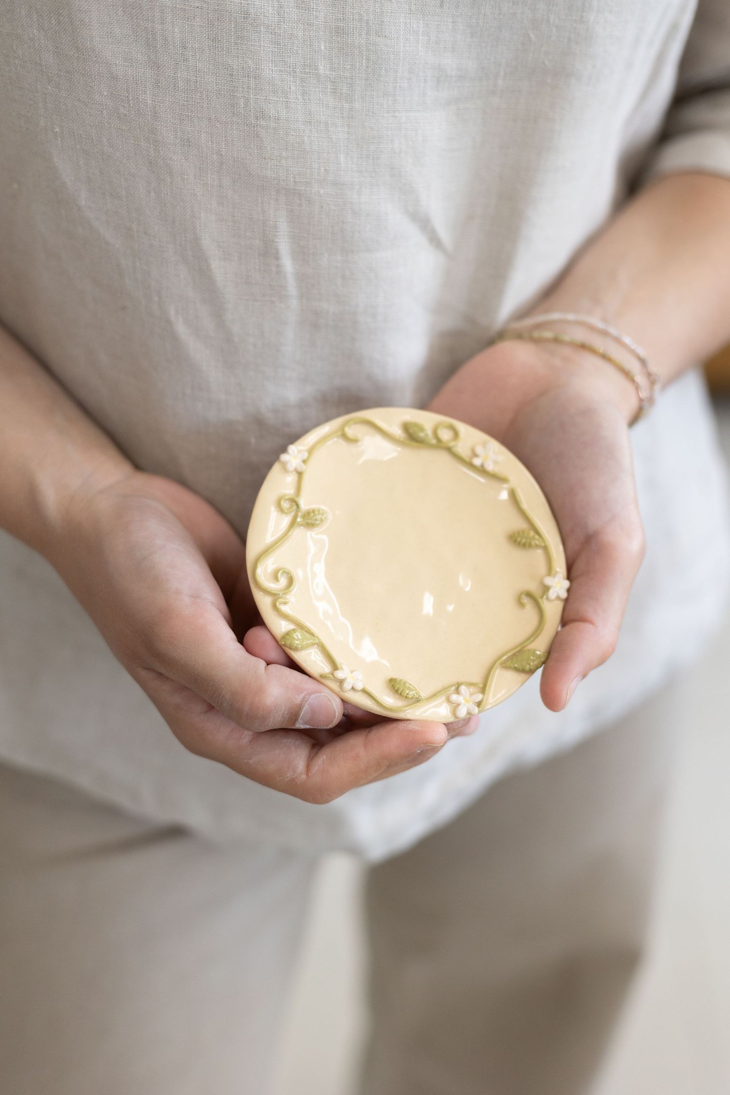 Hands holding a small decorative ceramic plate with floral design and yellow glaze.