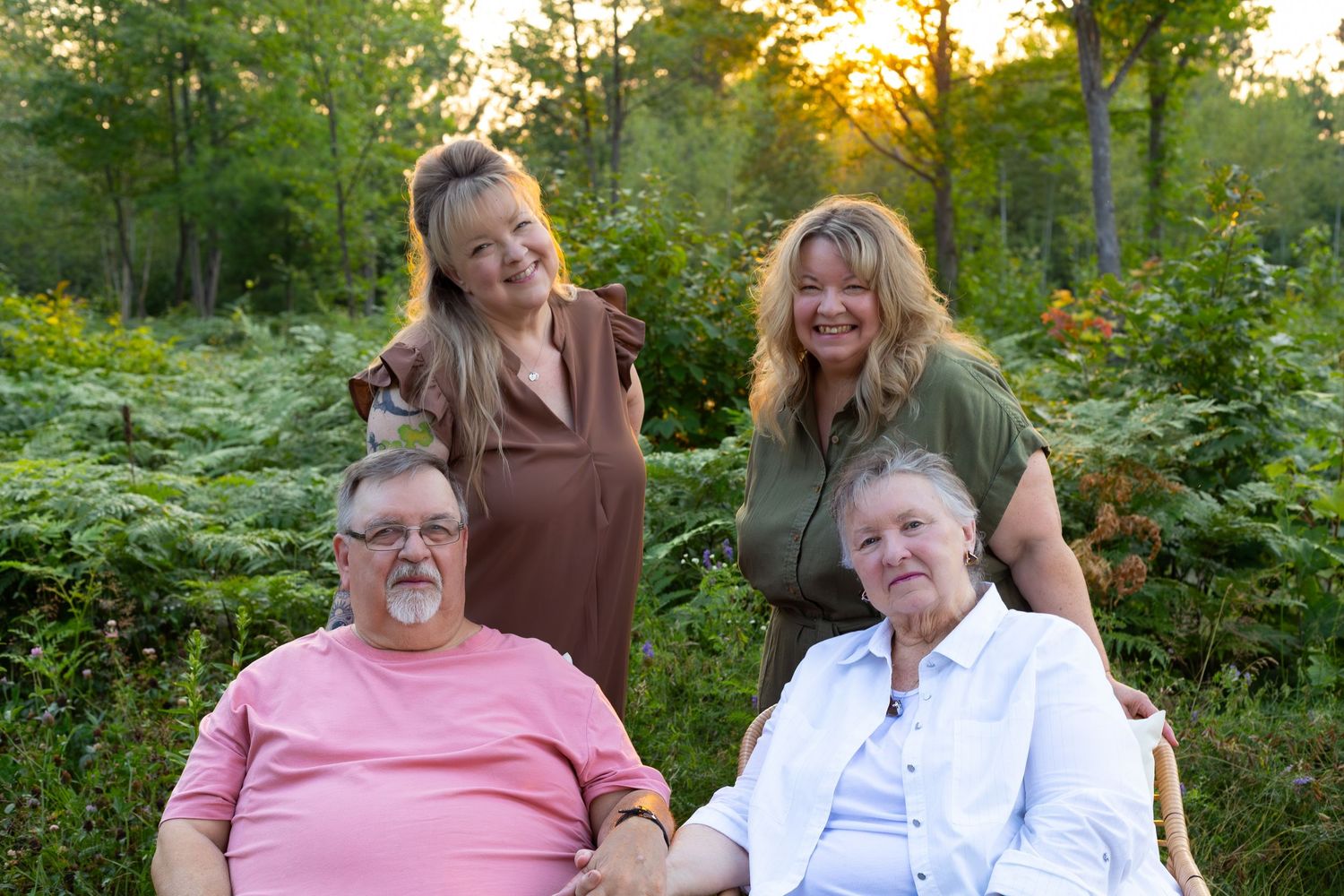 Four adults pose for portrait in lush green forest at golden hour sunset.