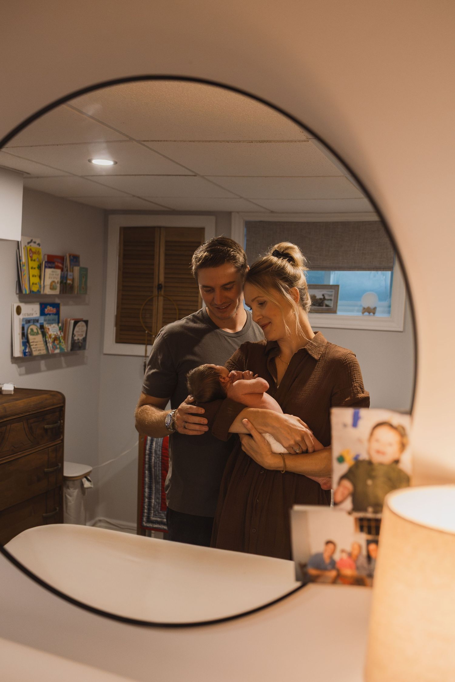 Couple admiring their newborn baby reflected in a round mirror in a cozy nursery room.