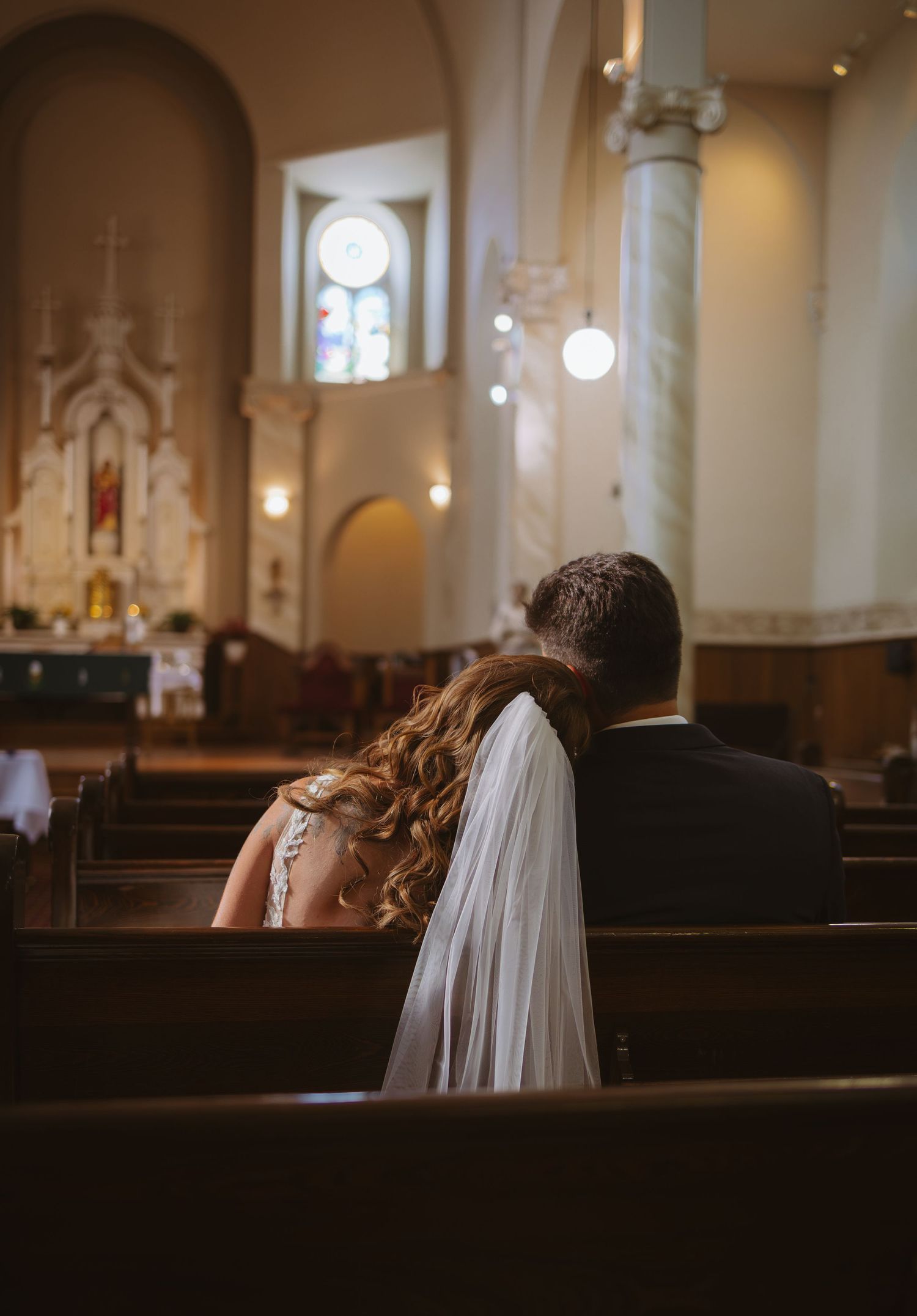 Bride and groom sitting together in a church pew during their wedding ceremony, with the altar visible in the background.