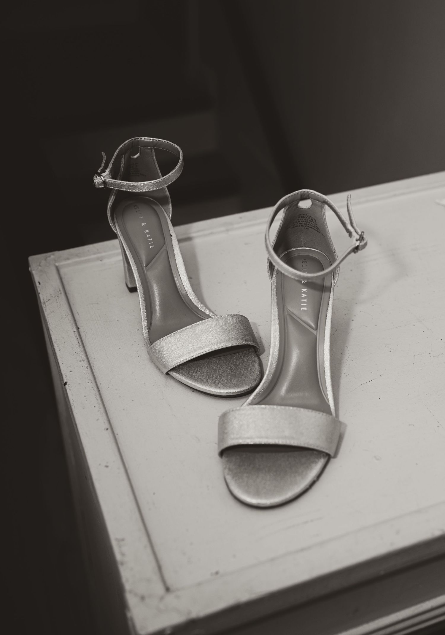 Black and white photo of elegant strappy heeled sandals placed on a white surface.