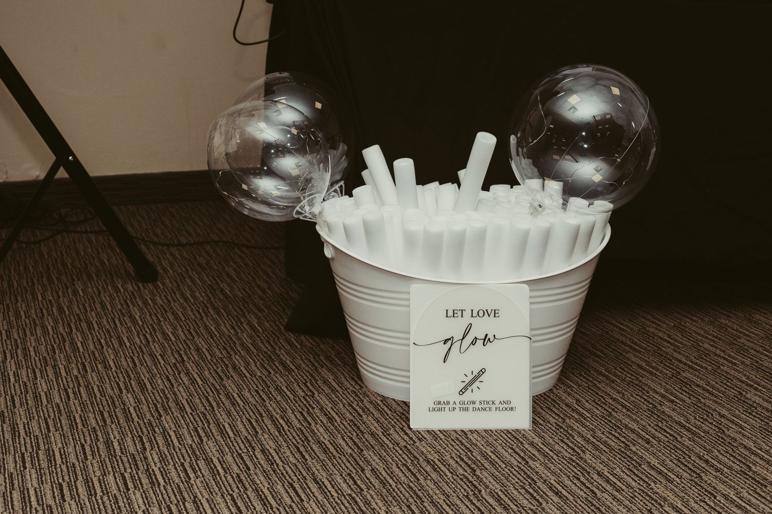 White bucket with glow sticks and Let Love Glow sign for wedding reception party favors.