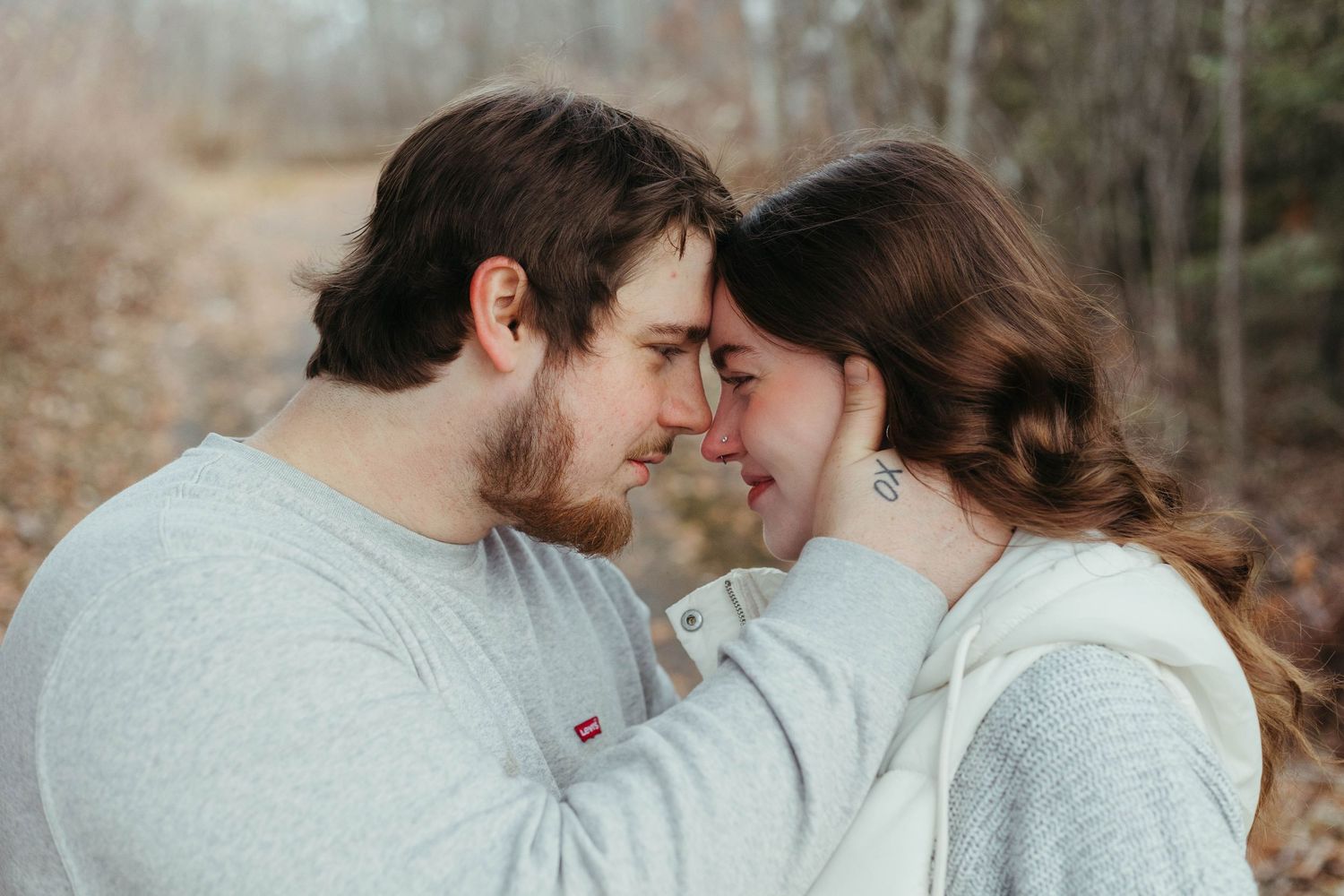 Loving couple touches foreheads gently in a soft romantic outdoor portrait among autumn trees.