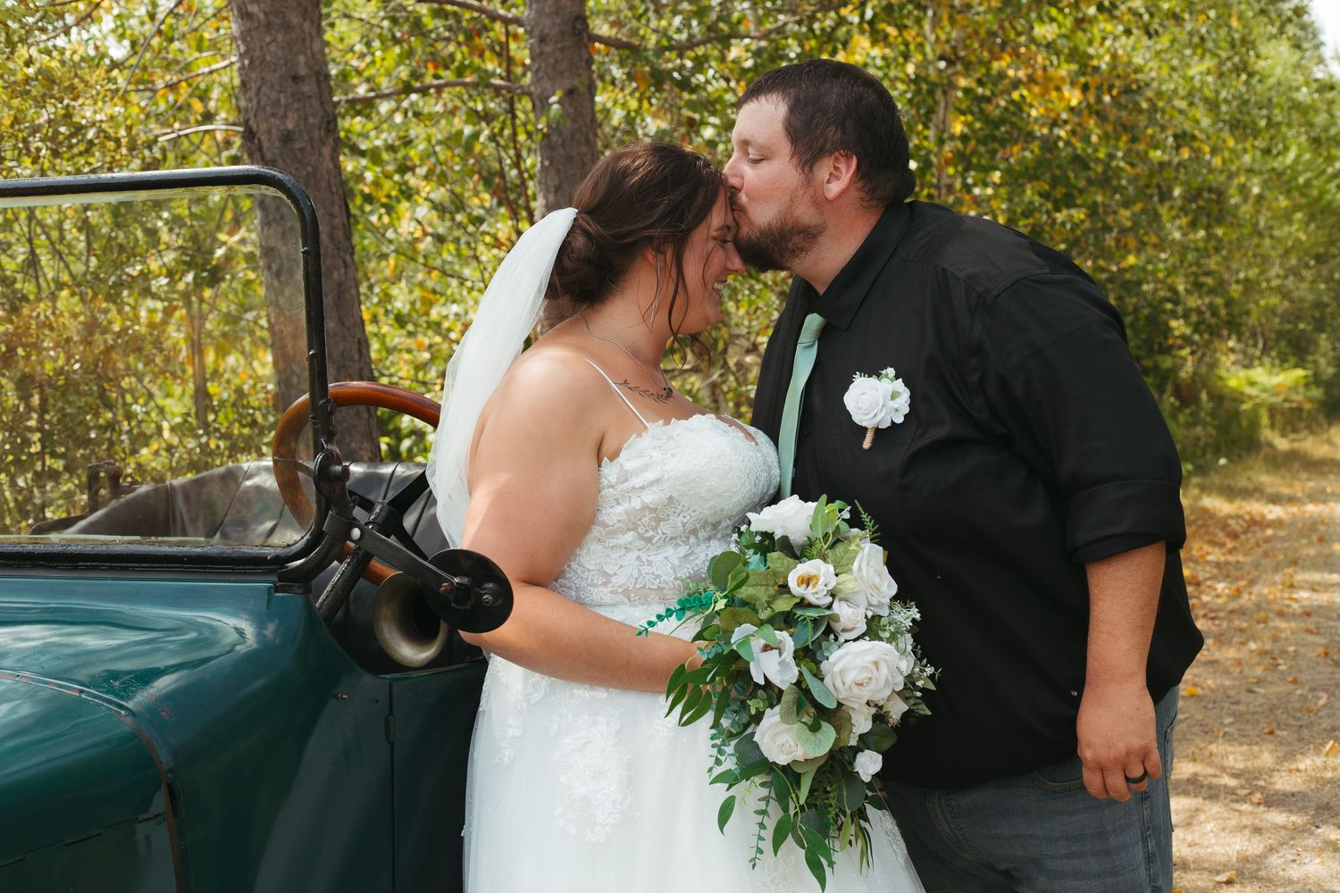 Bride and groom share a kiss beside a vintage green truck outdoors.