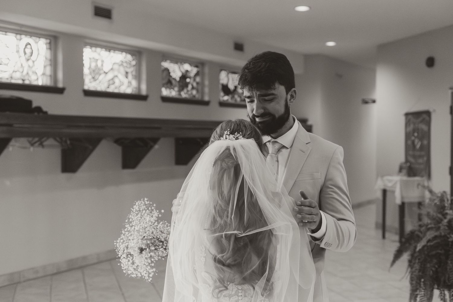 Black and white photo of groom lifting bride's veil during an intimate wedding moment in a church.