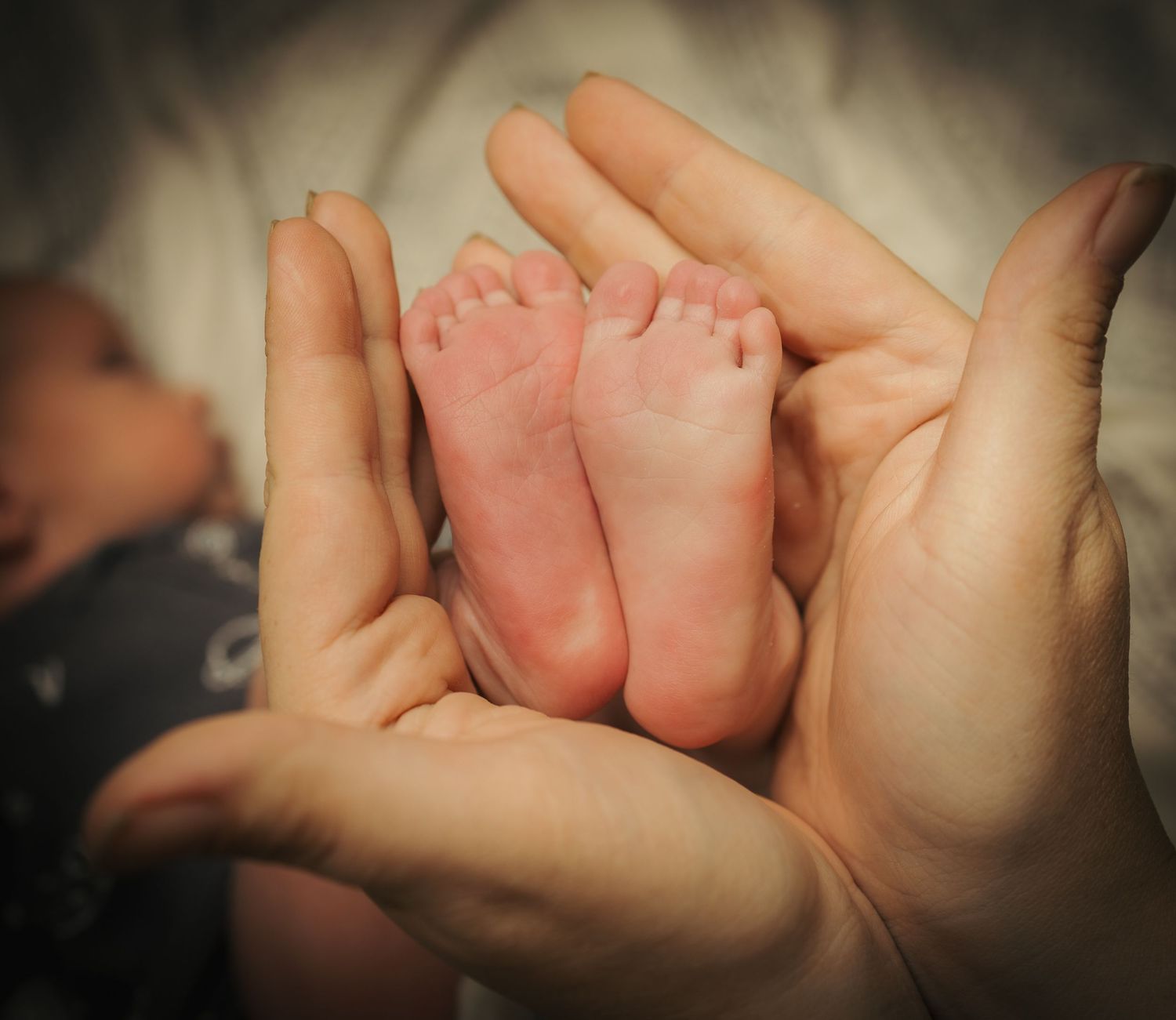 Adult hands gently cradling tiny newborn baby feet, showcasing the delicate size difference in a tender, loving moment.