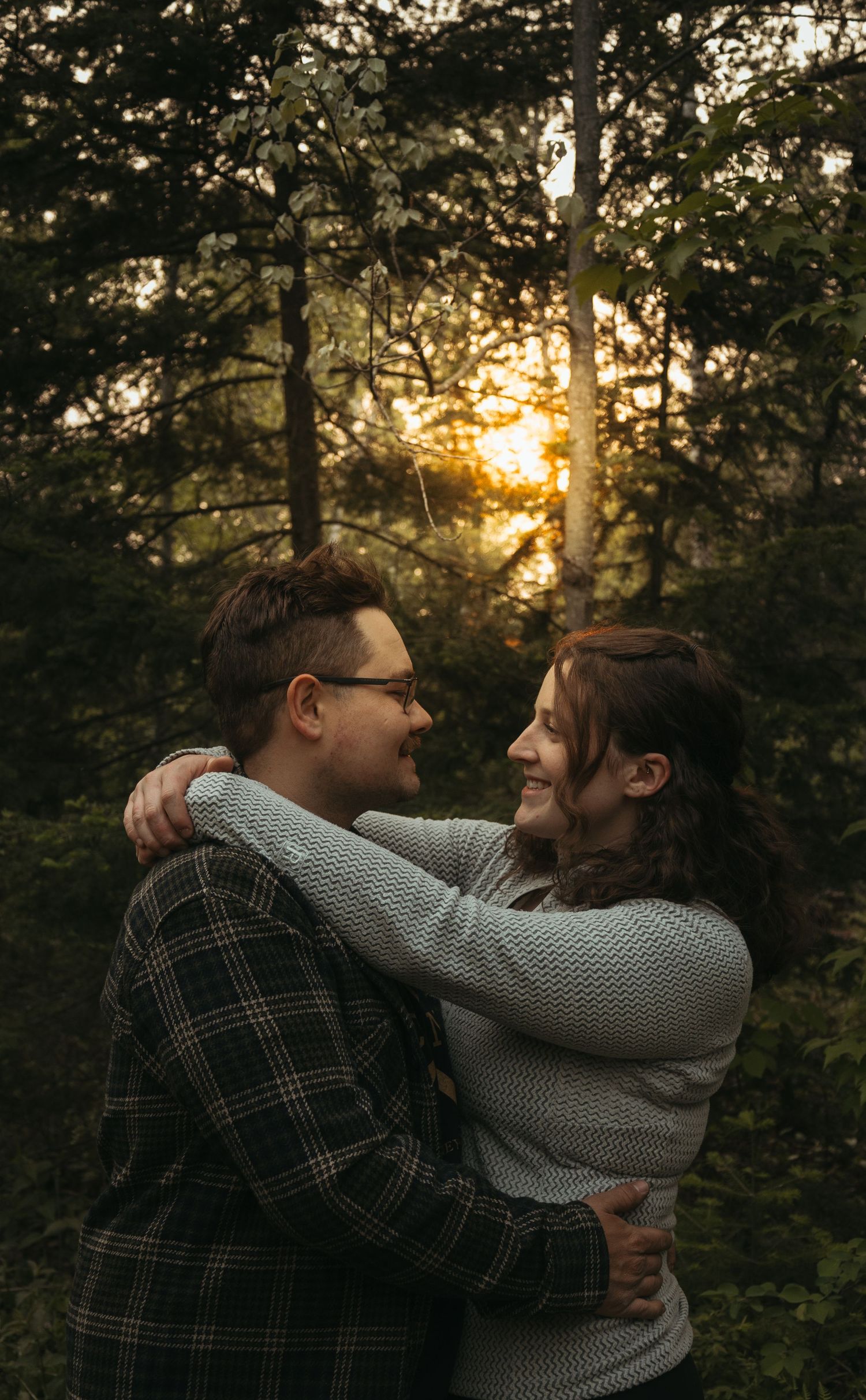 Happy couple embracing and smiling at each other with golden sunset light through trees.