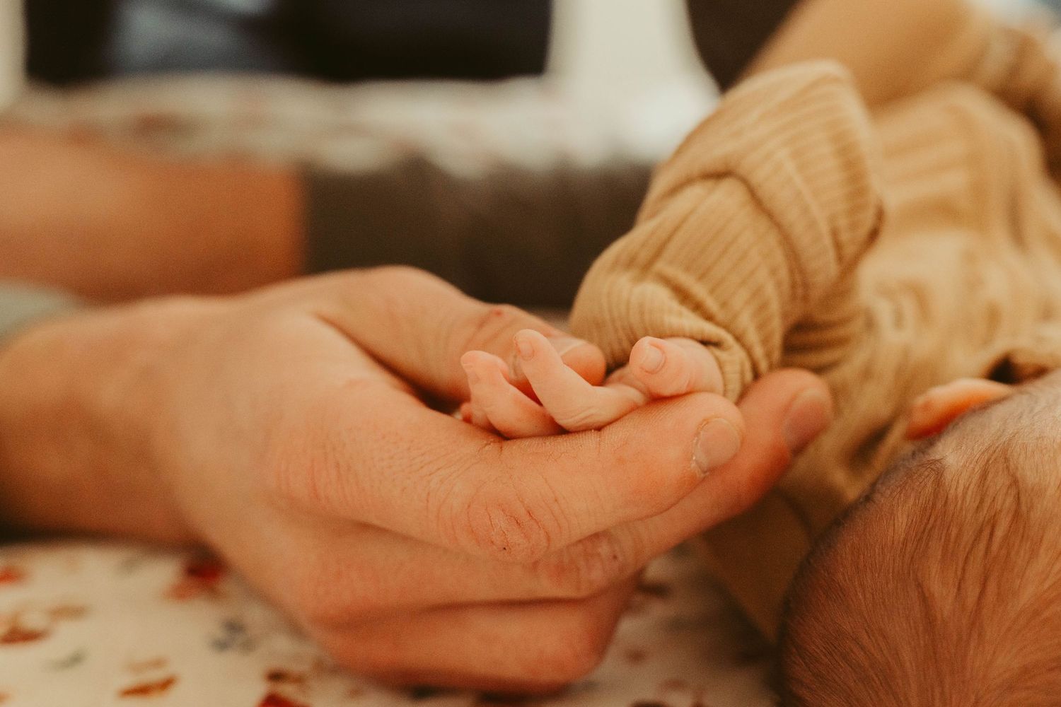 Close-up of a newborn baby gripping a parent's finger while wearing a knit outfit.