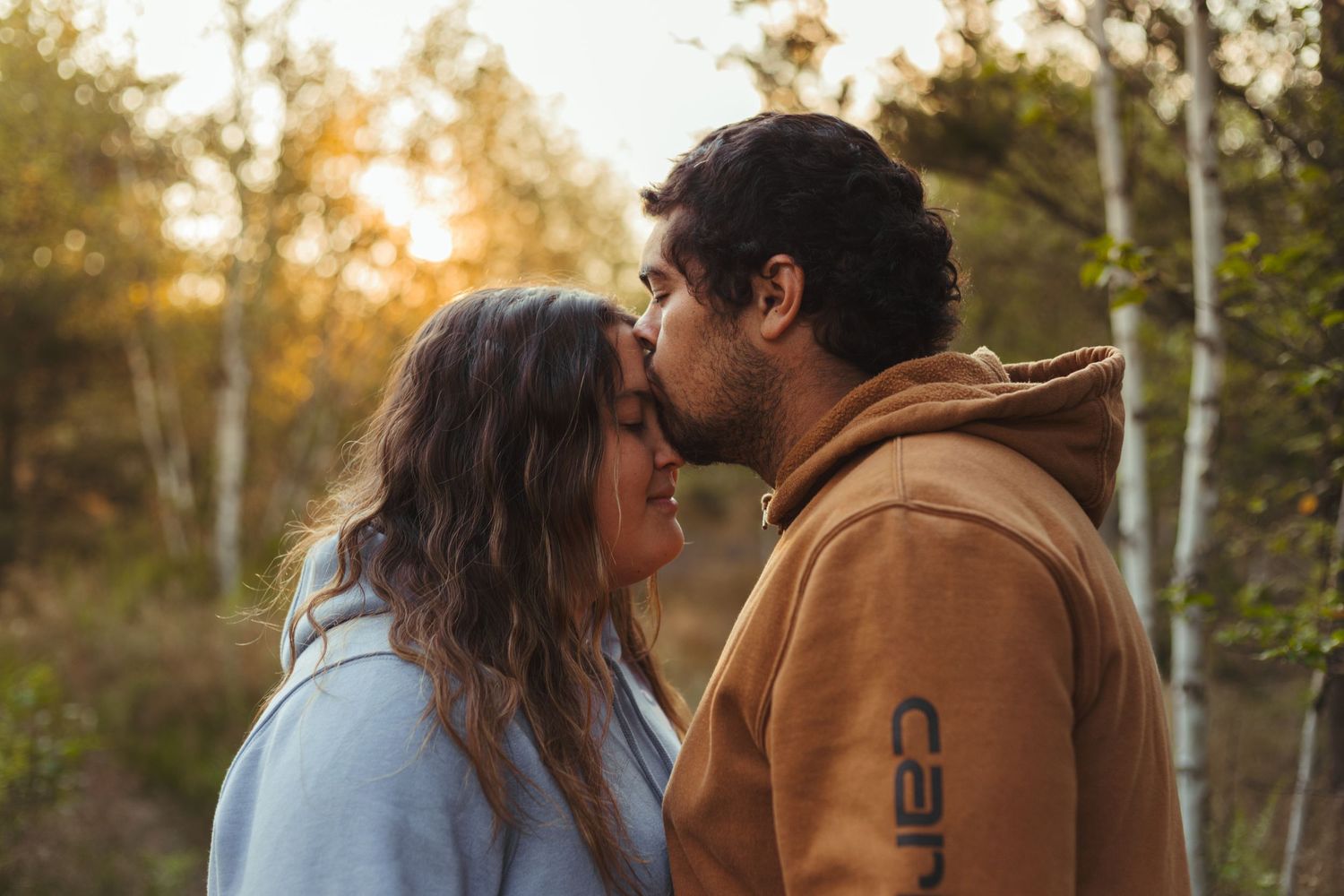 Couple sharing tender kiss outdoors surrounded by golden autumn birch trees.