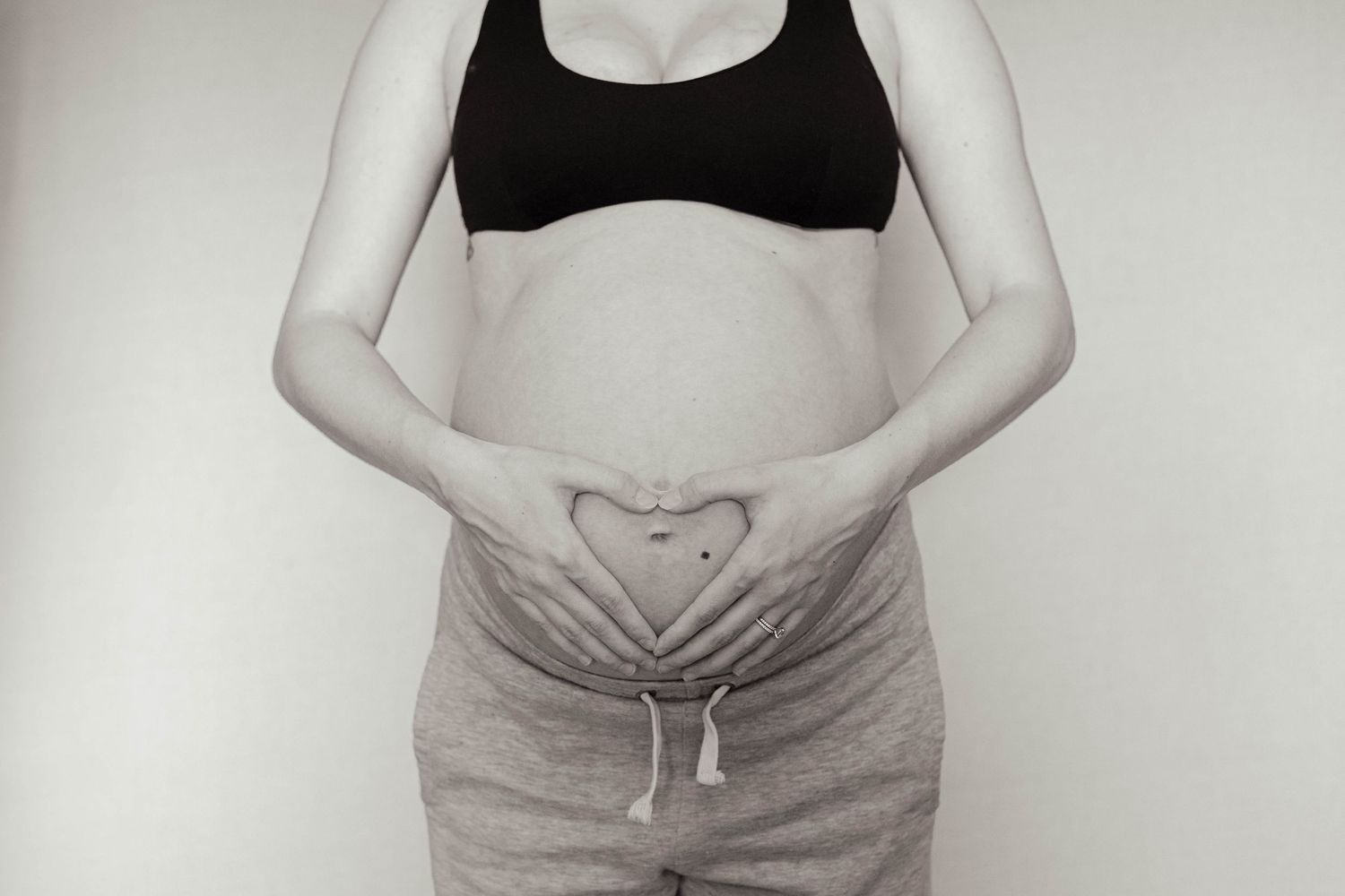 Black and white maternity photo of pregnant woman making heart shape with hands on baby bump.
