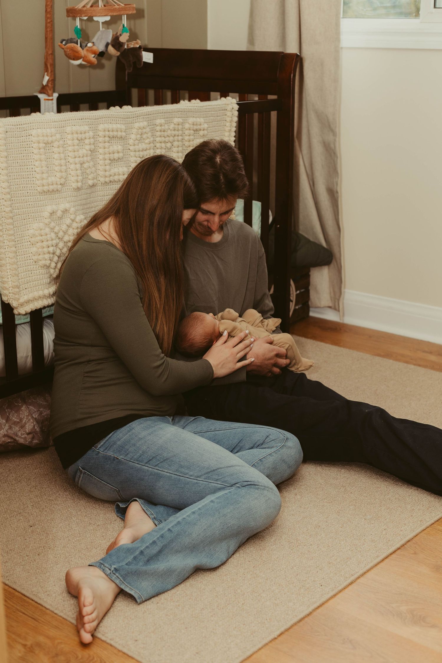 Young couple sitting on nursery floor together lovingly gazing at their newborn baby.