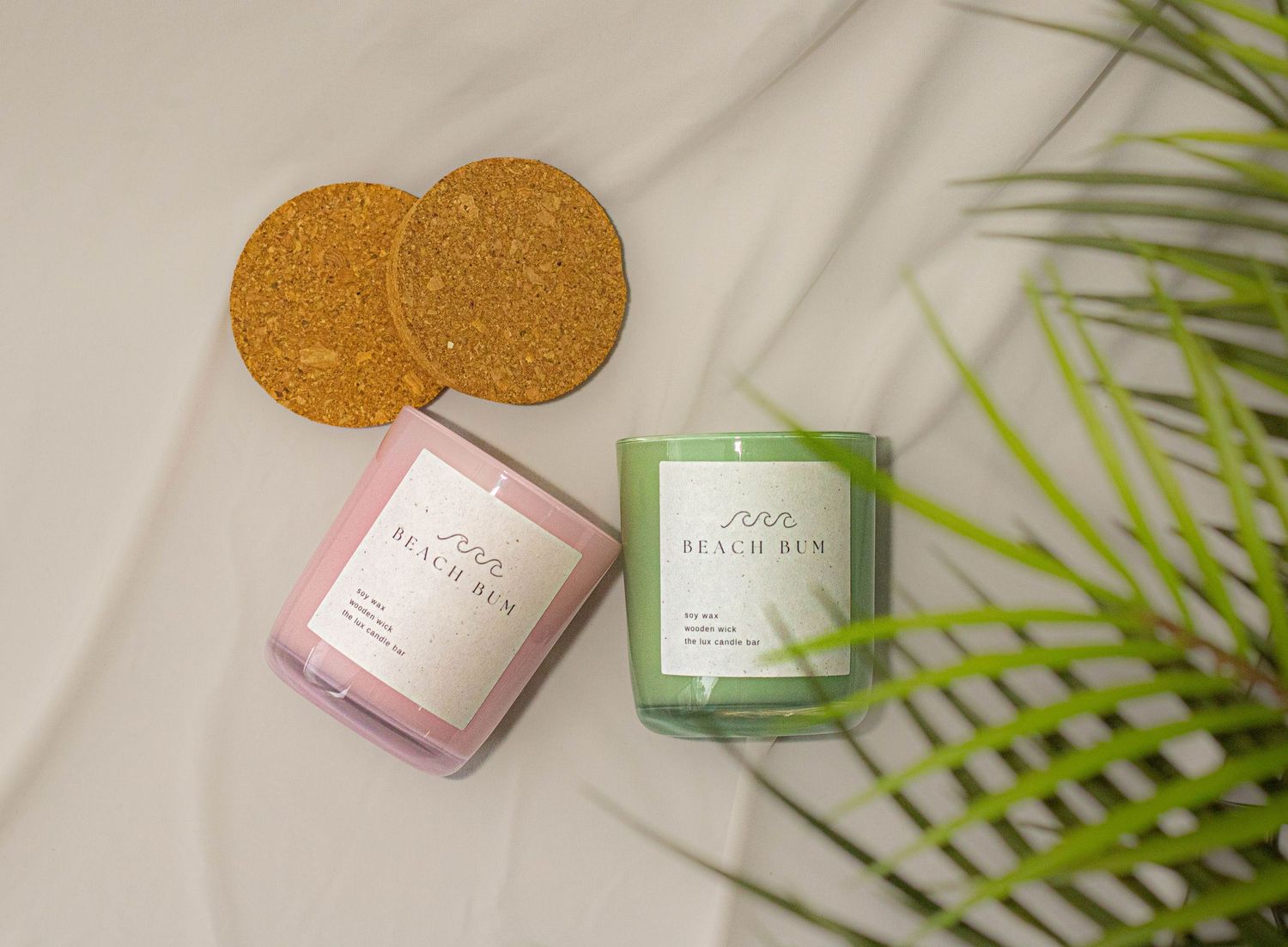 Beach Bum scented candles in pink and green glass jars with cork coasters and palm leaves.