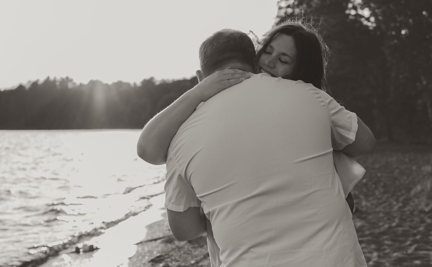 Couple sharing a tender embrace on a beach at sunset in black and white photo.
