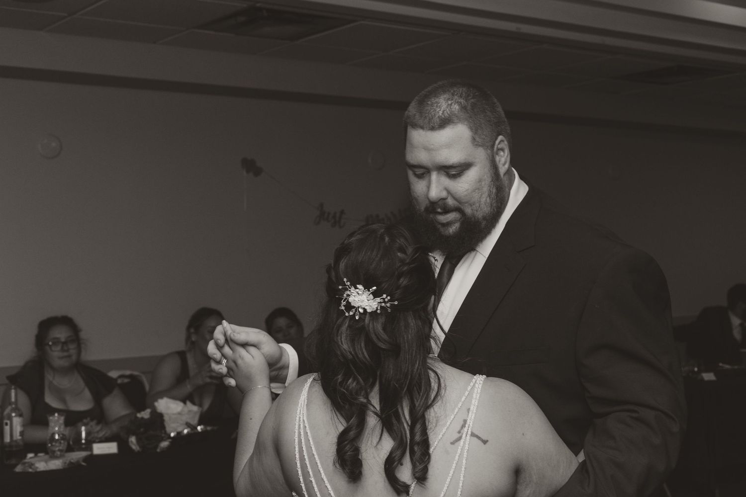 Black and white wedding reception photo of groom tenderly dancing with bride under soft lighting.