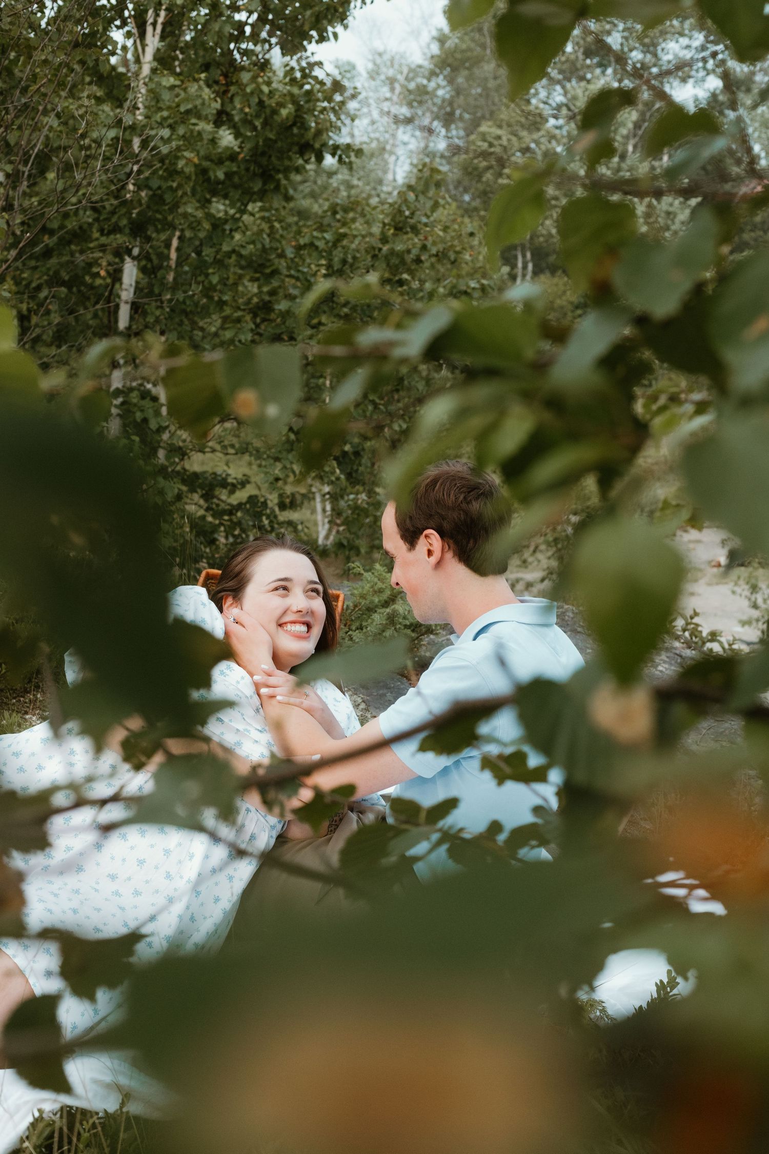 Happy couple smiling at each other surrounded by lush green foliage outdoors.