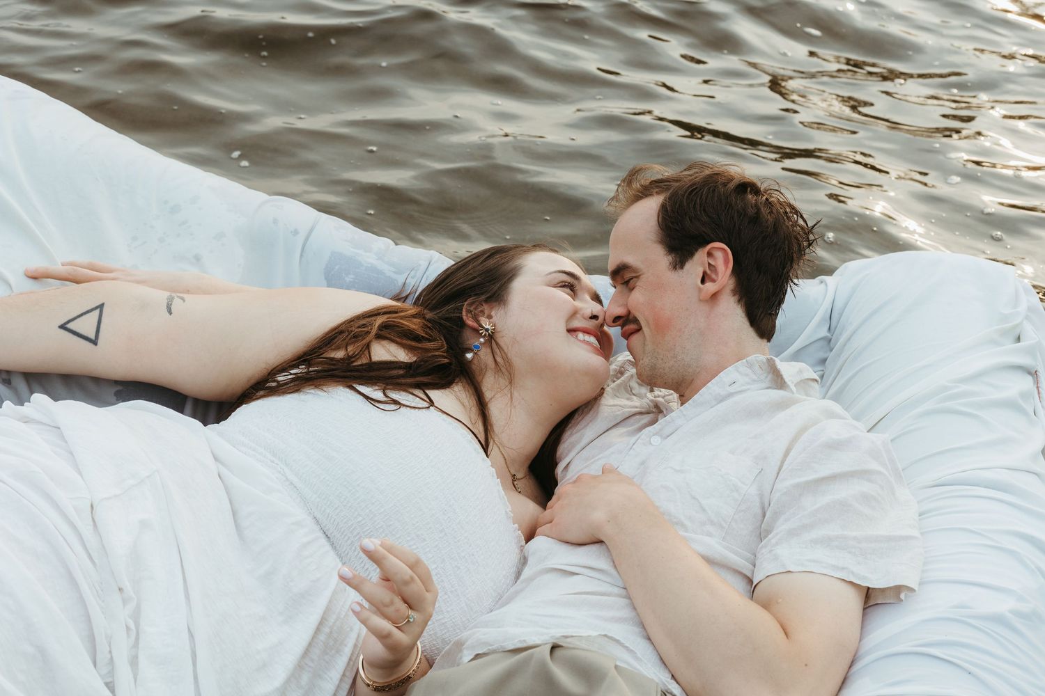 Happy couple lying together on white sheets floating on calm water.