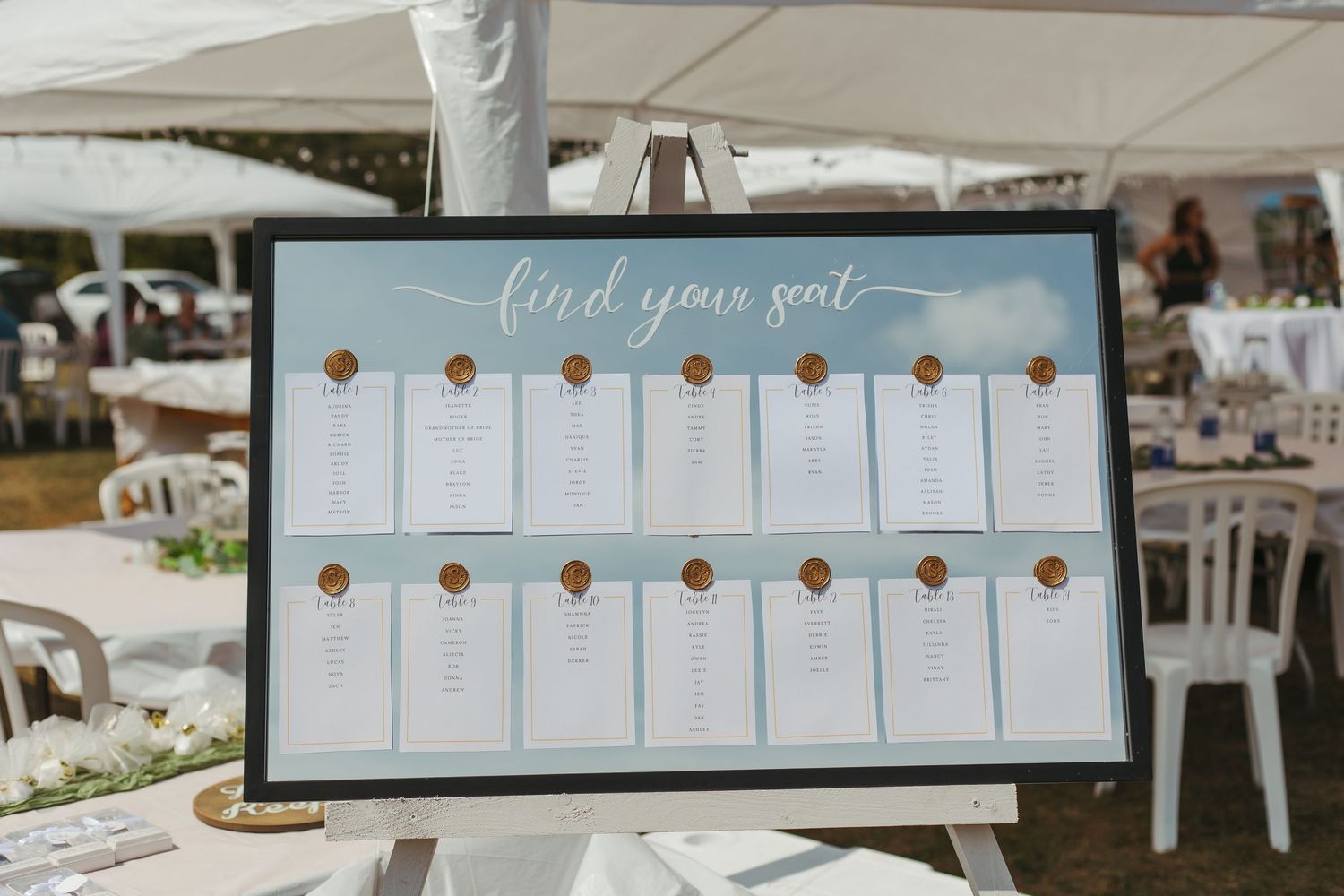 Elegant wedding seating chart with wax seals displayed on easel at reception.