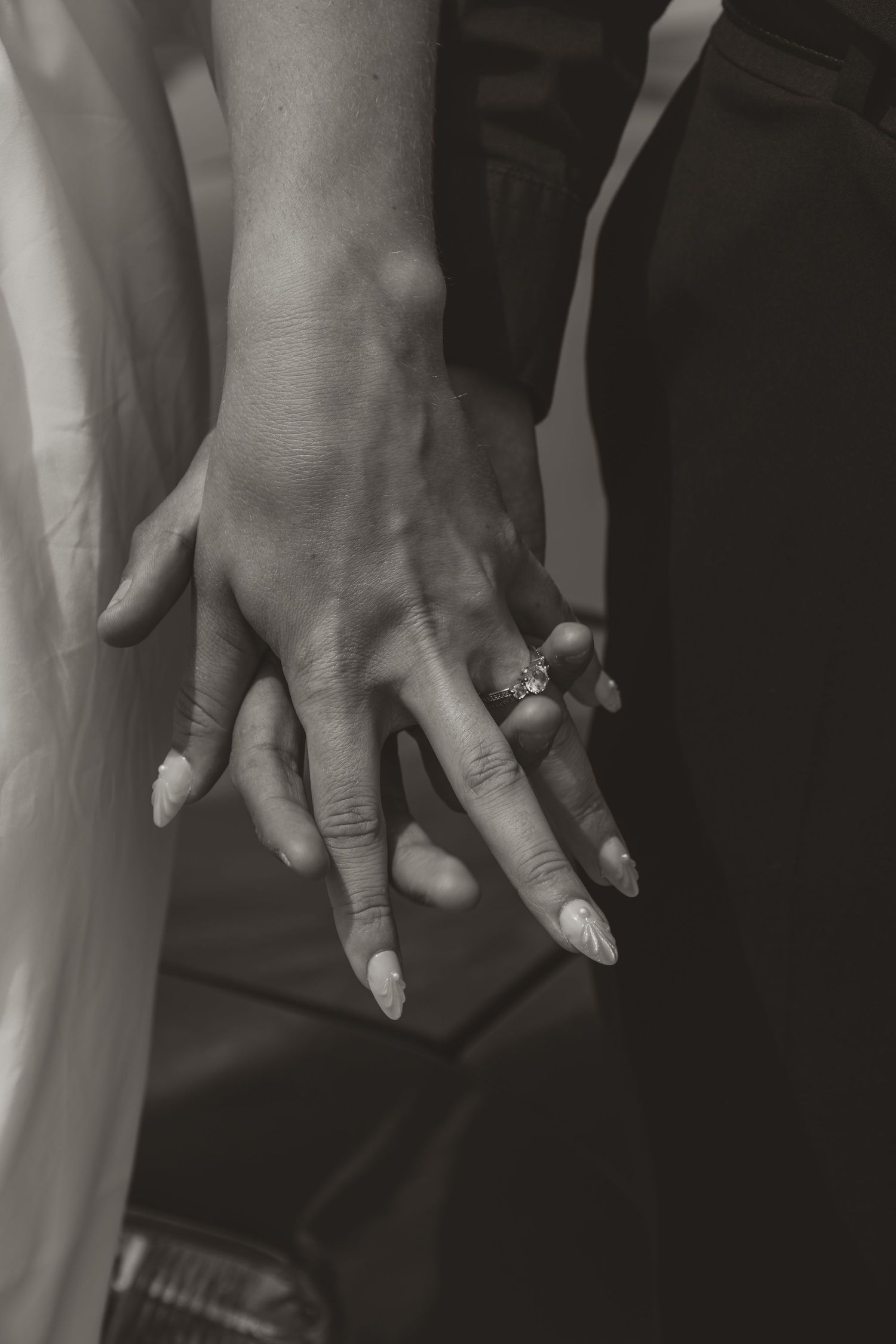 Black and white close-up of couple holding hands with sparkling engagement ring.