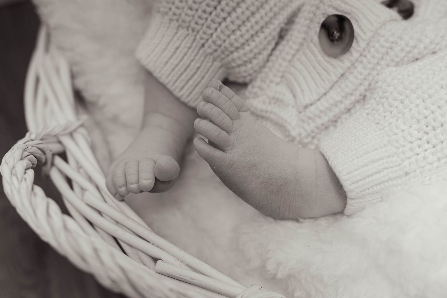 Black and white close-up of a newborn baby's tiny feet peeking out from a knit outfit in a basket.