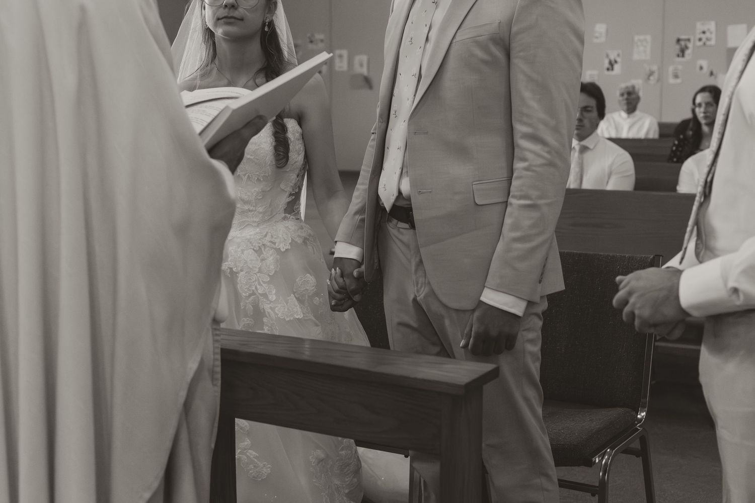 Black and white photo of bride and groom holding hands at the altar during their church wedding ceremony.