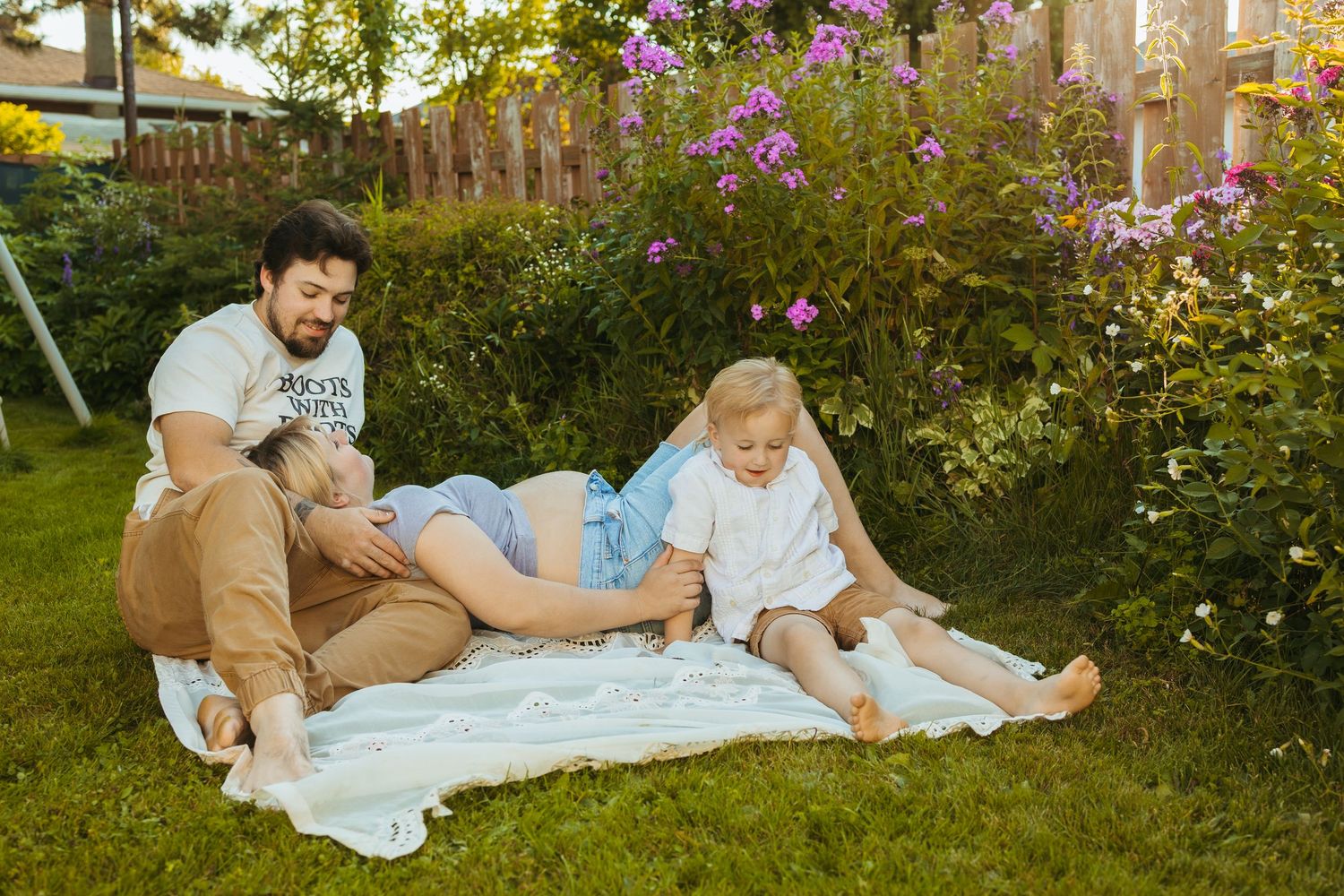 Happy family with pregnant mother relaxing on blanket in sunny garden with toddler and partner.