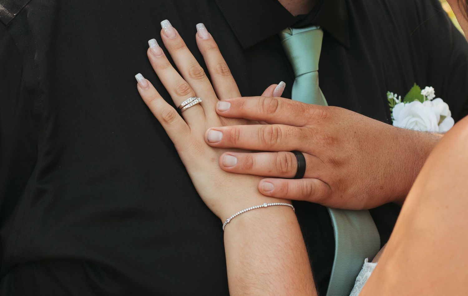 Close-up of bride and groom hands showing wedding rings, groom wearing mint green tie.