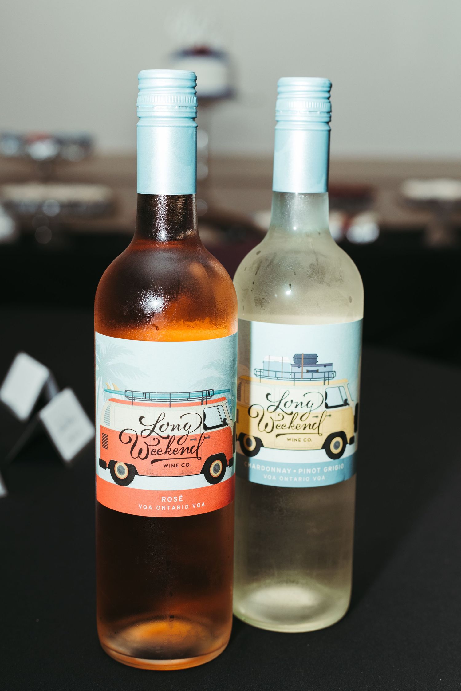 Two Long Weekend Wine Co. bottles, rosé and white, displayed on a black tablecloth at an event.