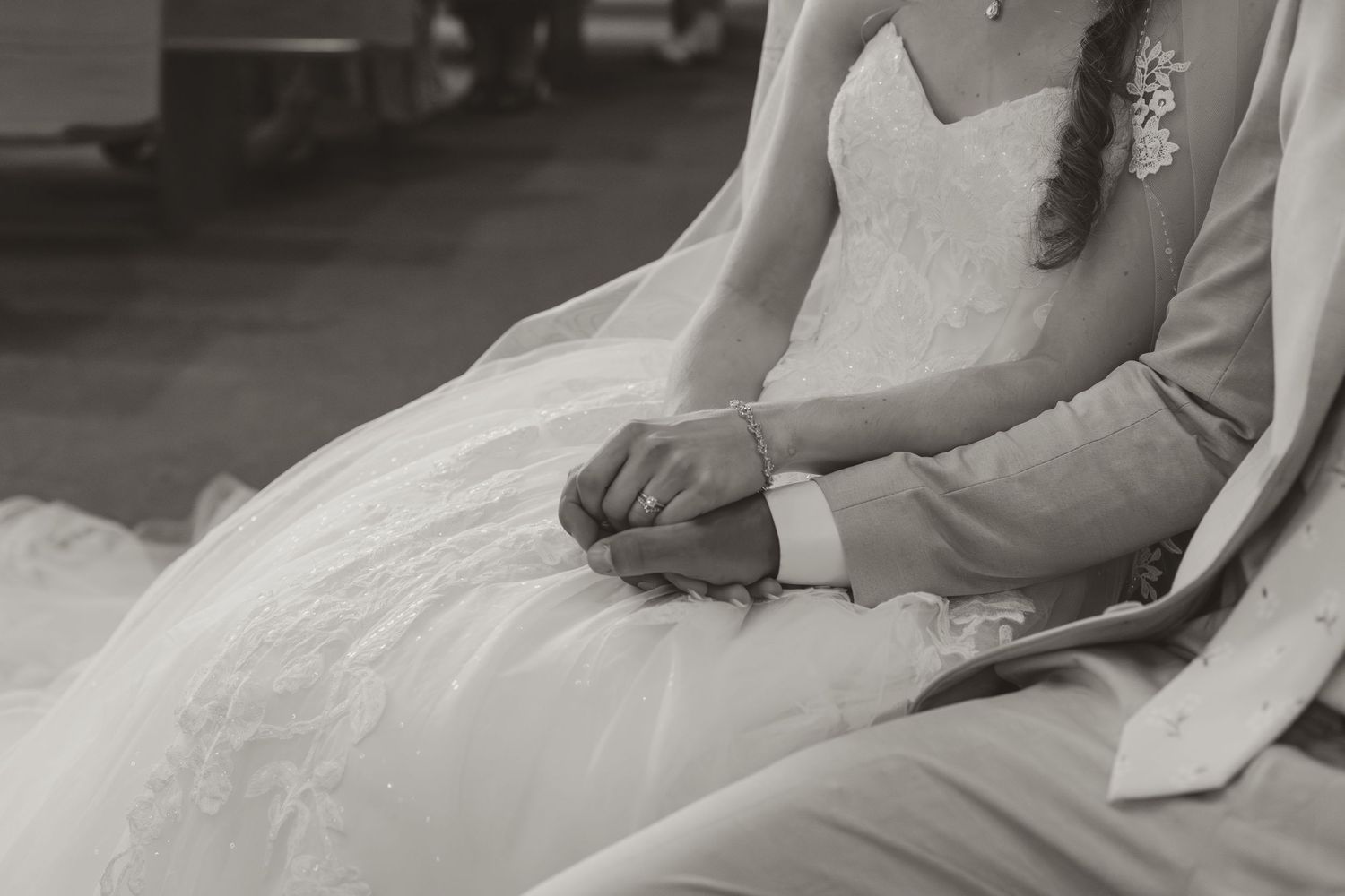 Black and white close-up of bride and groom holding hands in wedding attire on their special day.