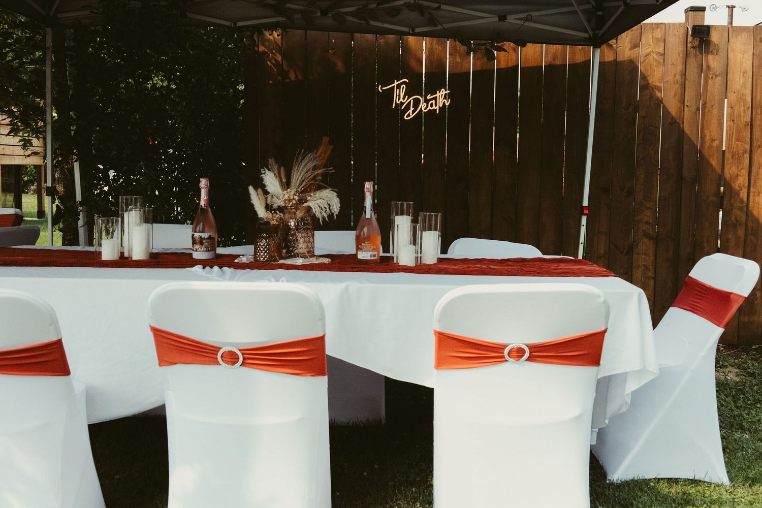 Elegant outdoor wedding reception table with white chairs and orange satin sashes.