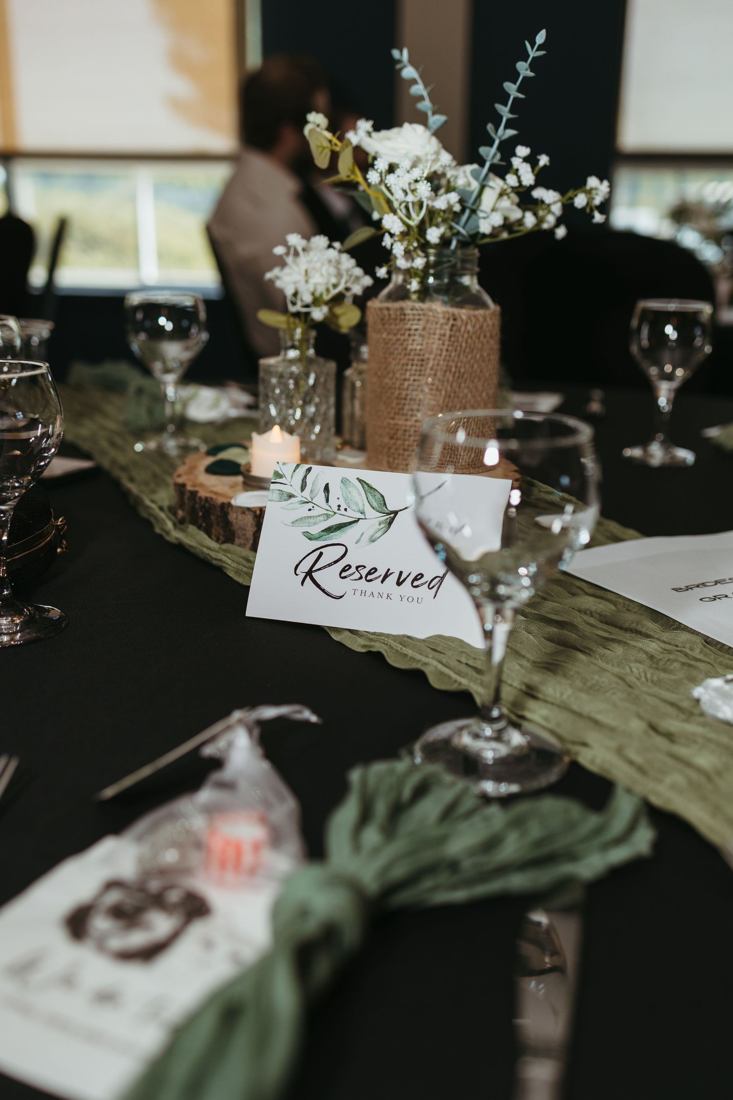 Elegant wedding reception table with Reserved sign, greenery runner, floral centerpiece, and crystal glassware.