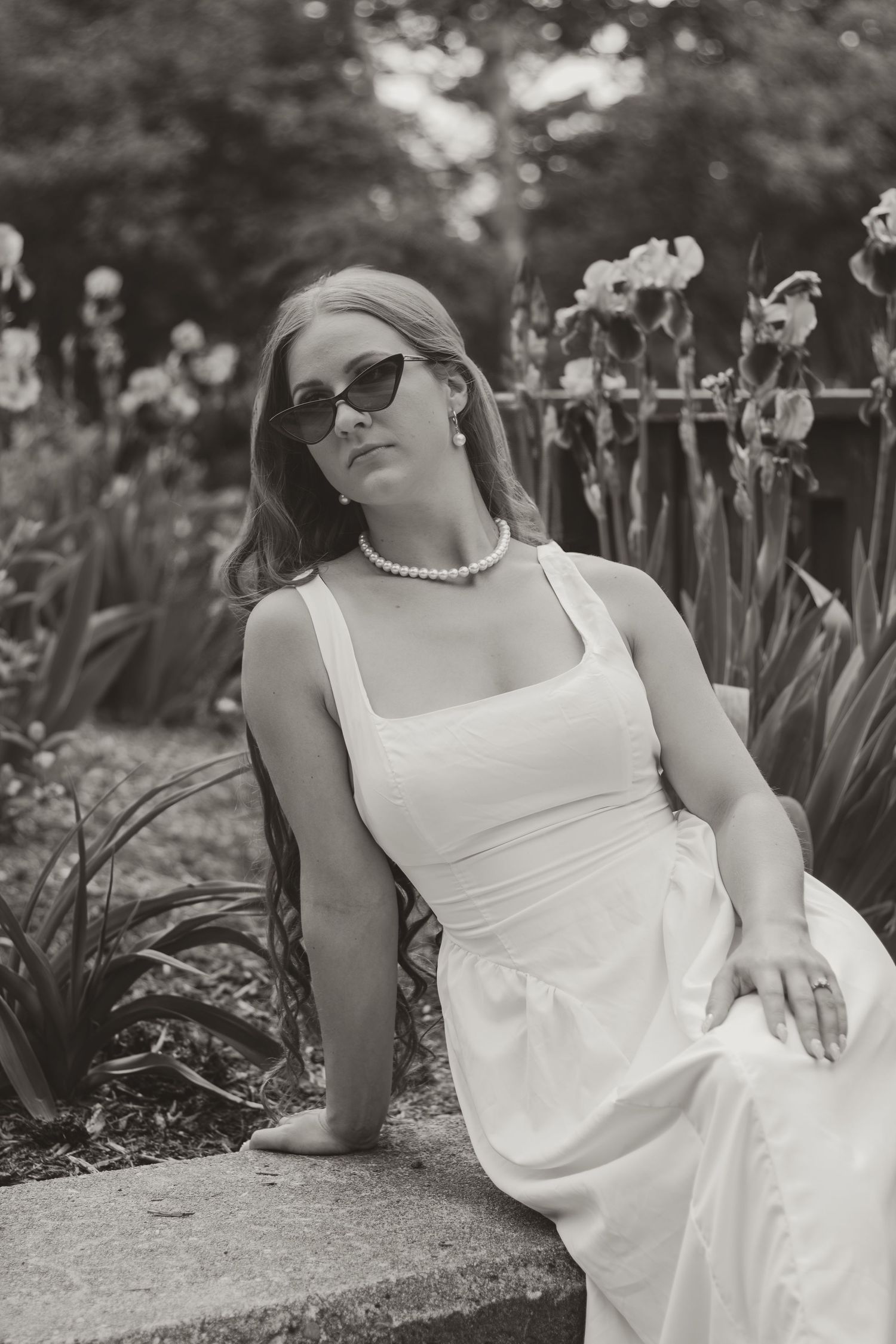 Vintage black and white photo of woman in white dress and sunglasses in garden.